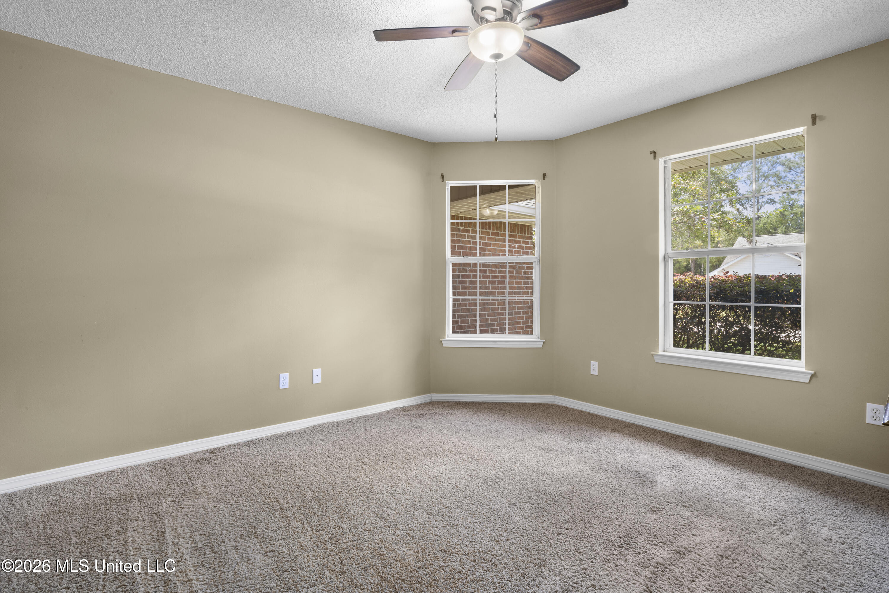 Empty bedroom with beige walls, carpet, two windows, and a ceiling fan.