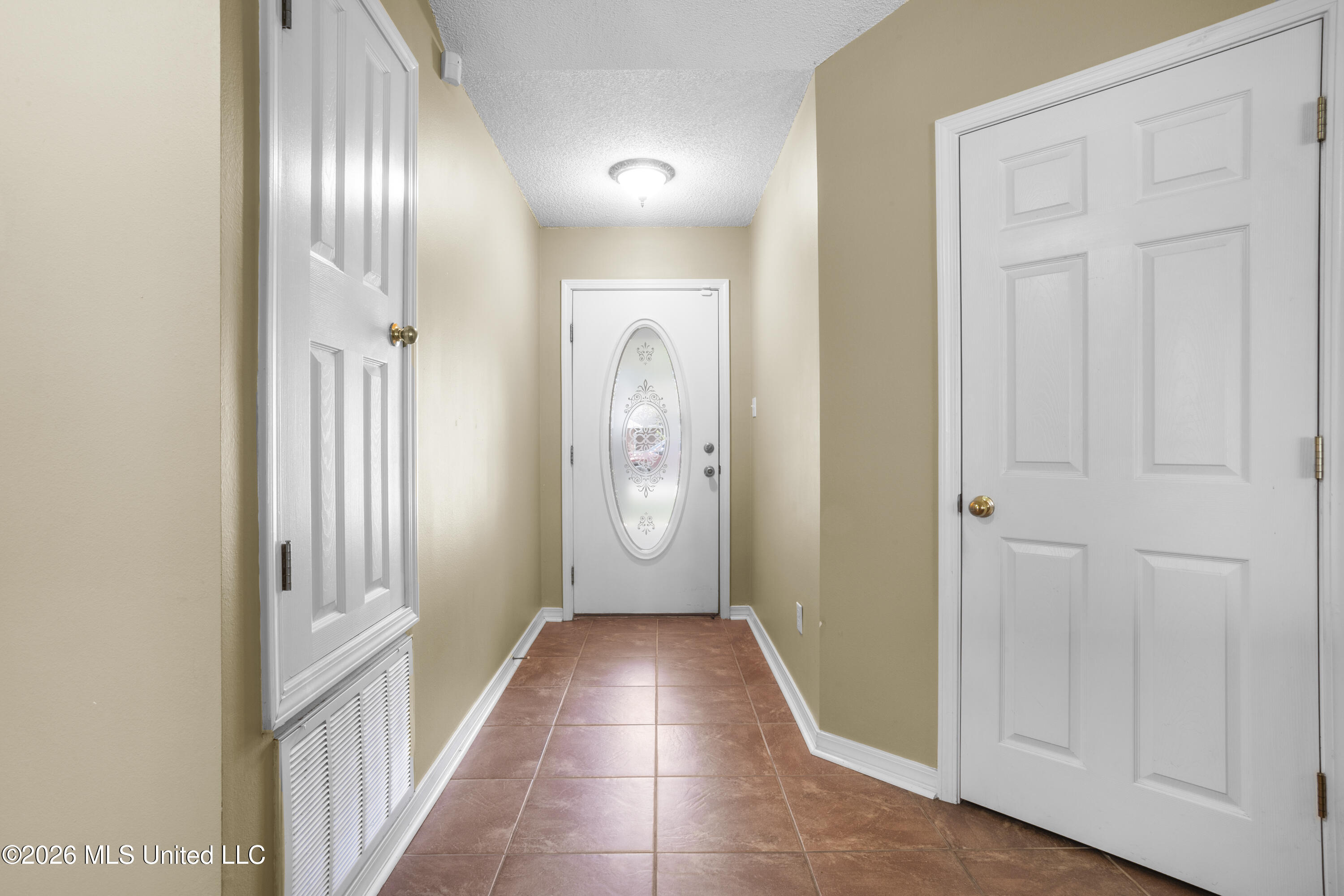Entry hall with terracotta-colored tile and a white front door with oval decorative glass.