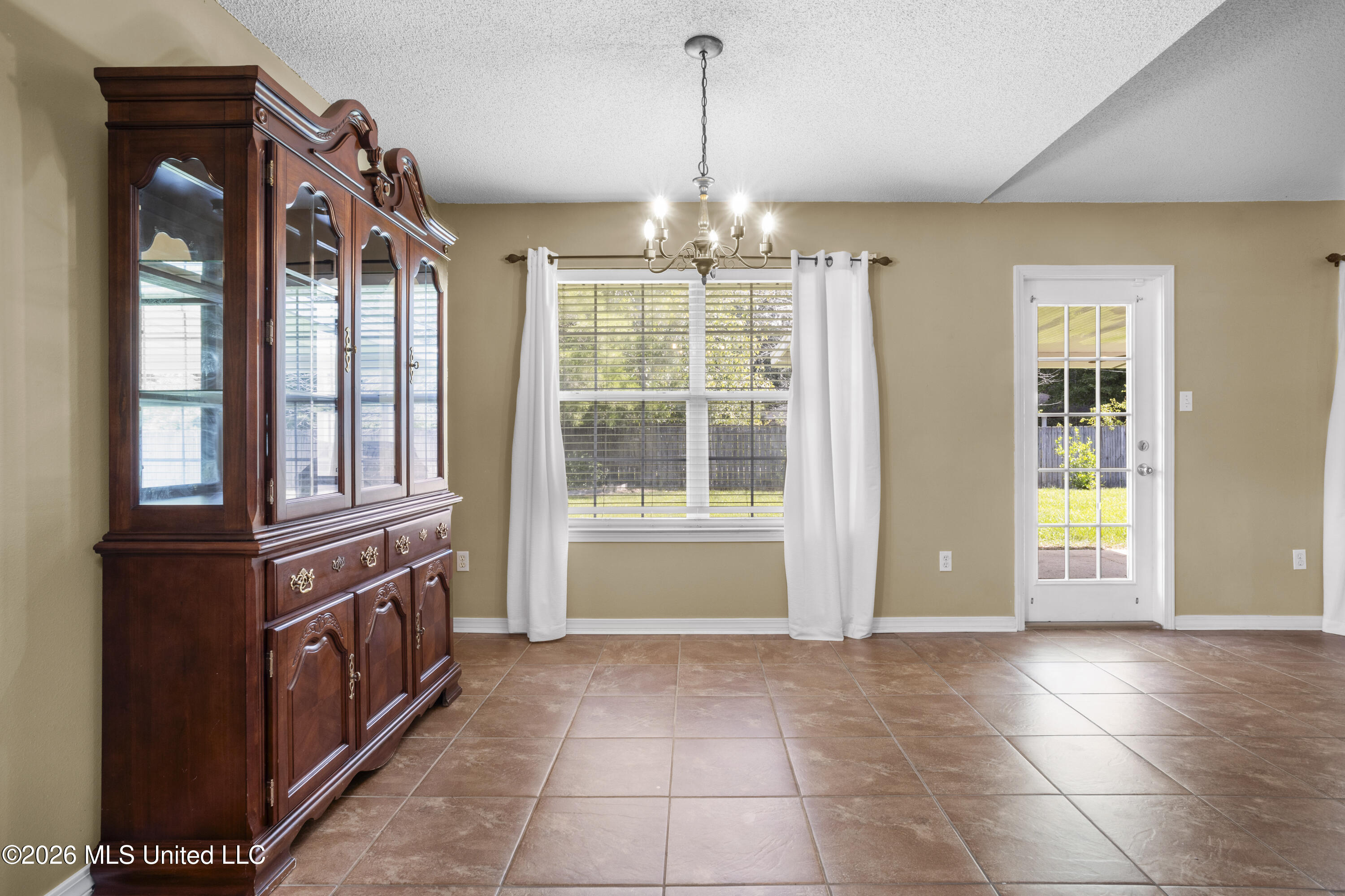 Dining room with a dark wood china cabinet, tiled floor, and chandelier beside a curtained window.