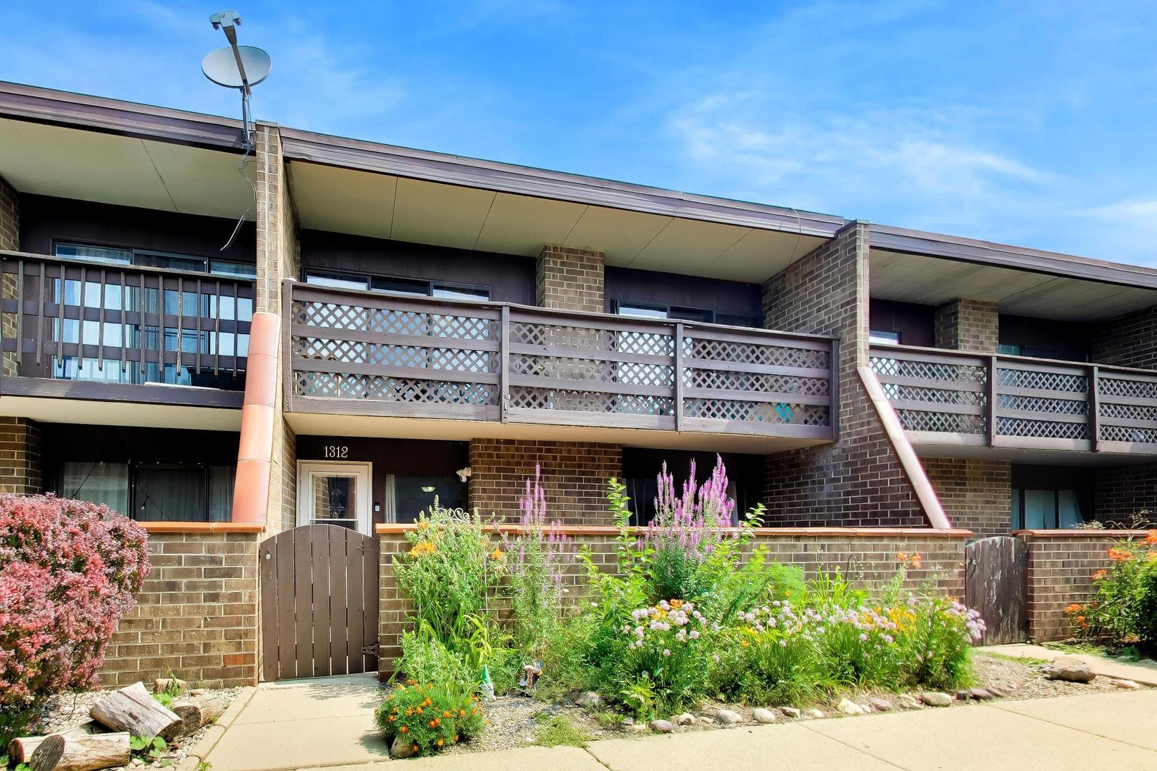 Brick residence with lattice balcony railings and a flower garden around the entrance.