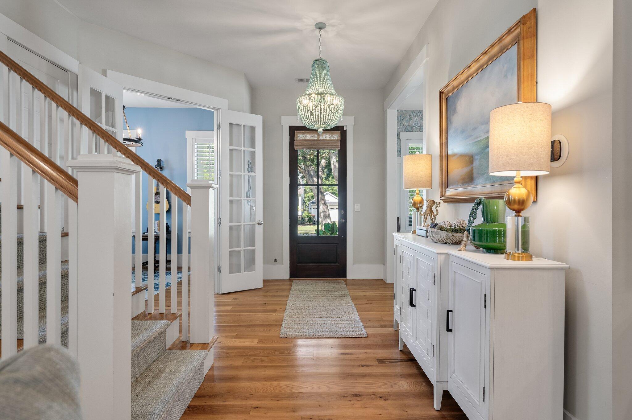 Entry foyer with a crystal chandelier, hardwood floors, and a white staircase beside a dark front door.