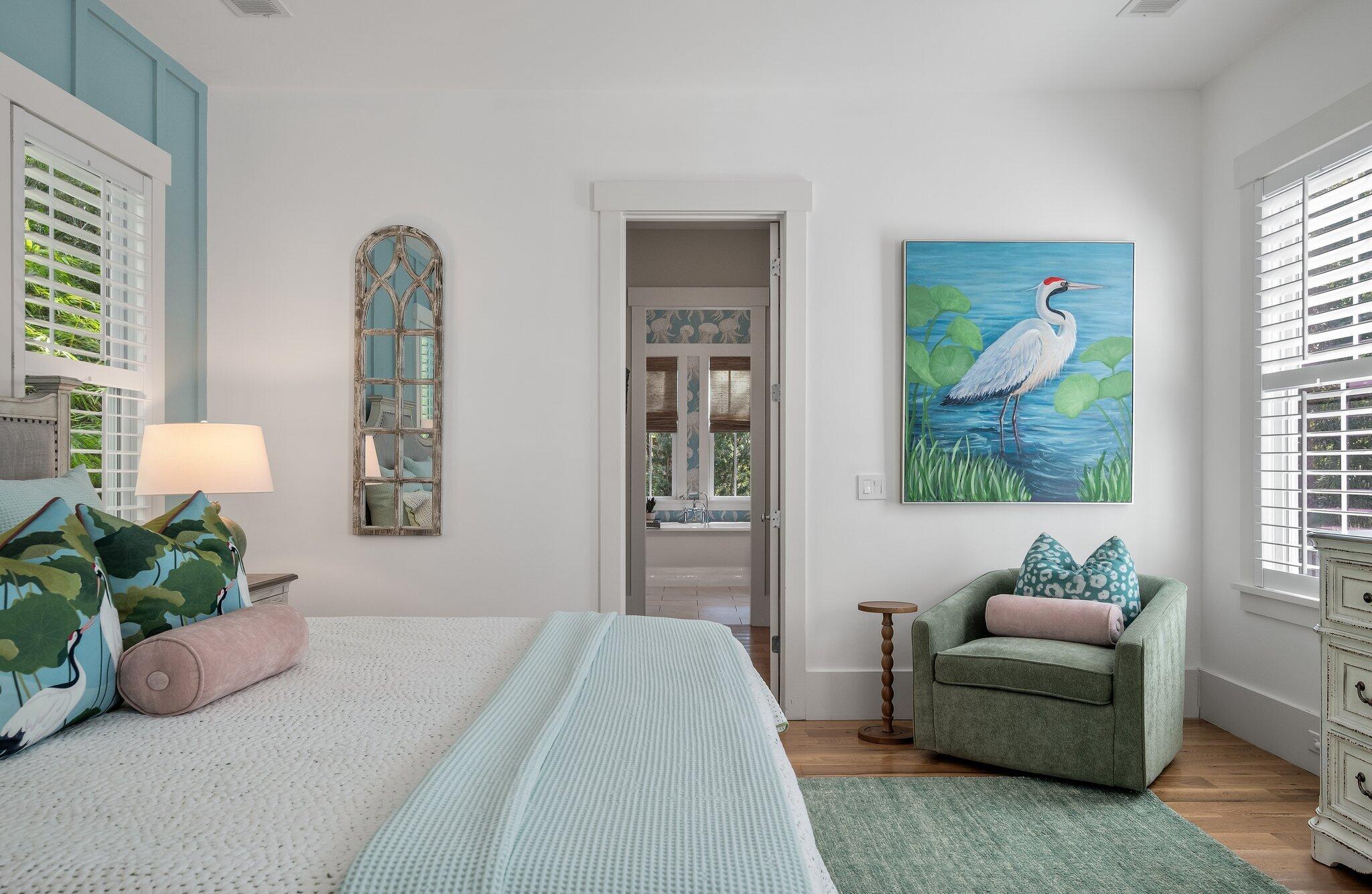 Bedroom with a white bed, aqua accents, green armchair, and heron painting.