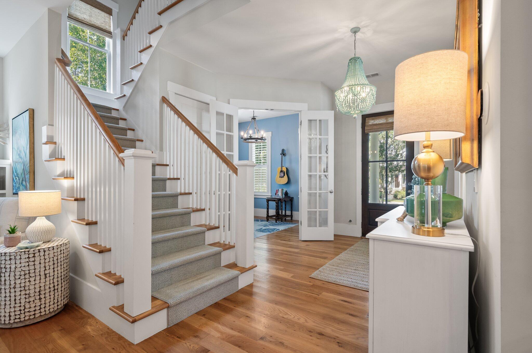 Furnished foyer with a carpeted staircase, wood handrails, chandelier, and open French doors to a blue room.