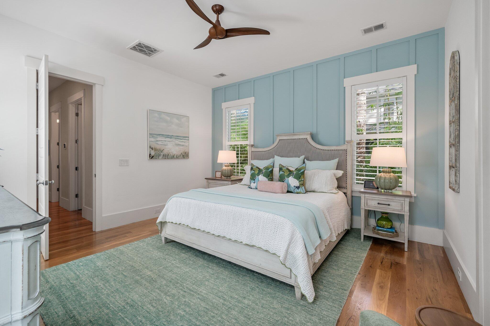 Bedroom with a white bed, blue paneled wall, shuttered windows, and teal rug.