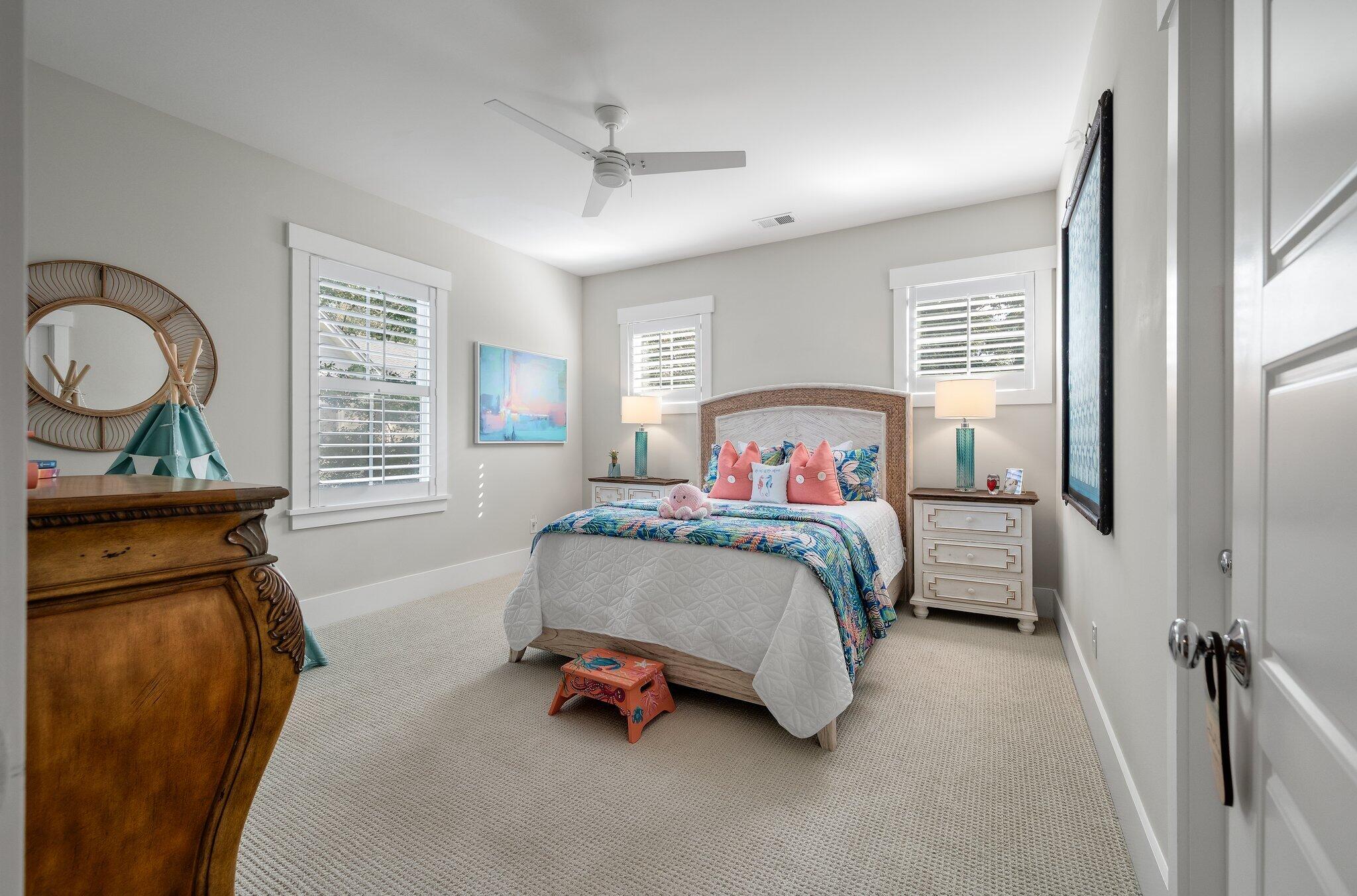 Furnished bedroom with colorful bedding, coral pillows, and plantation shutters.