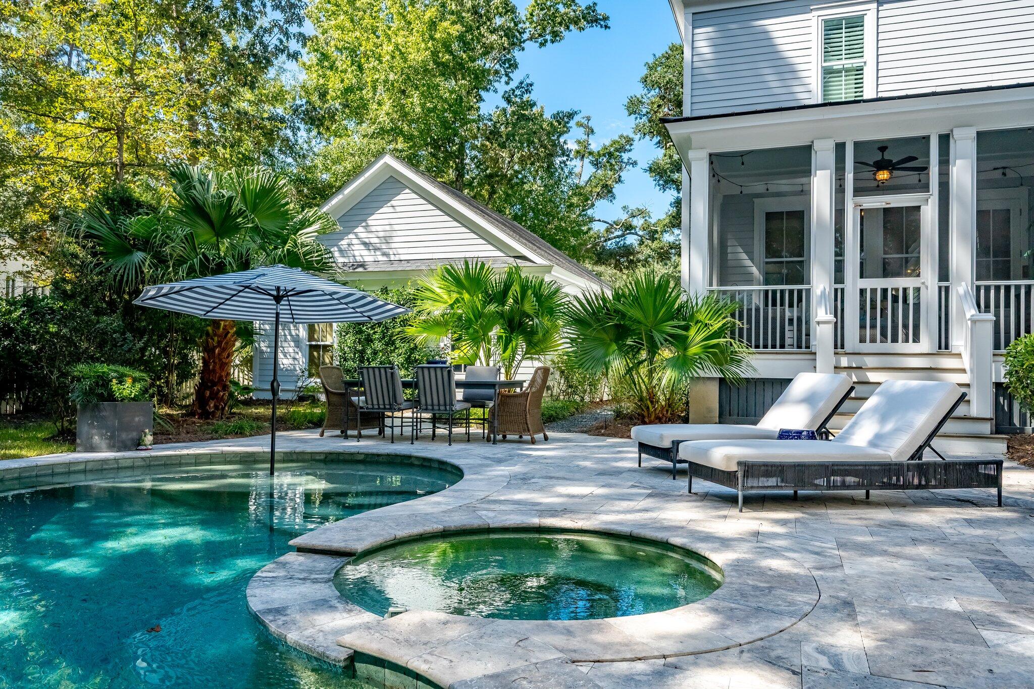 Backyard pool and circular spa beside a furnished stone patio and covered porch.