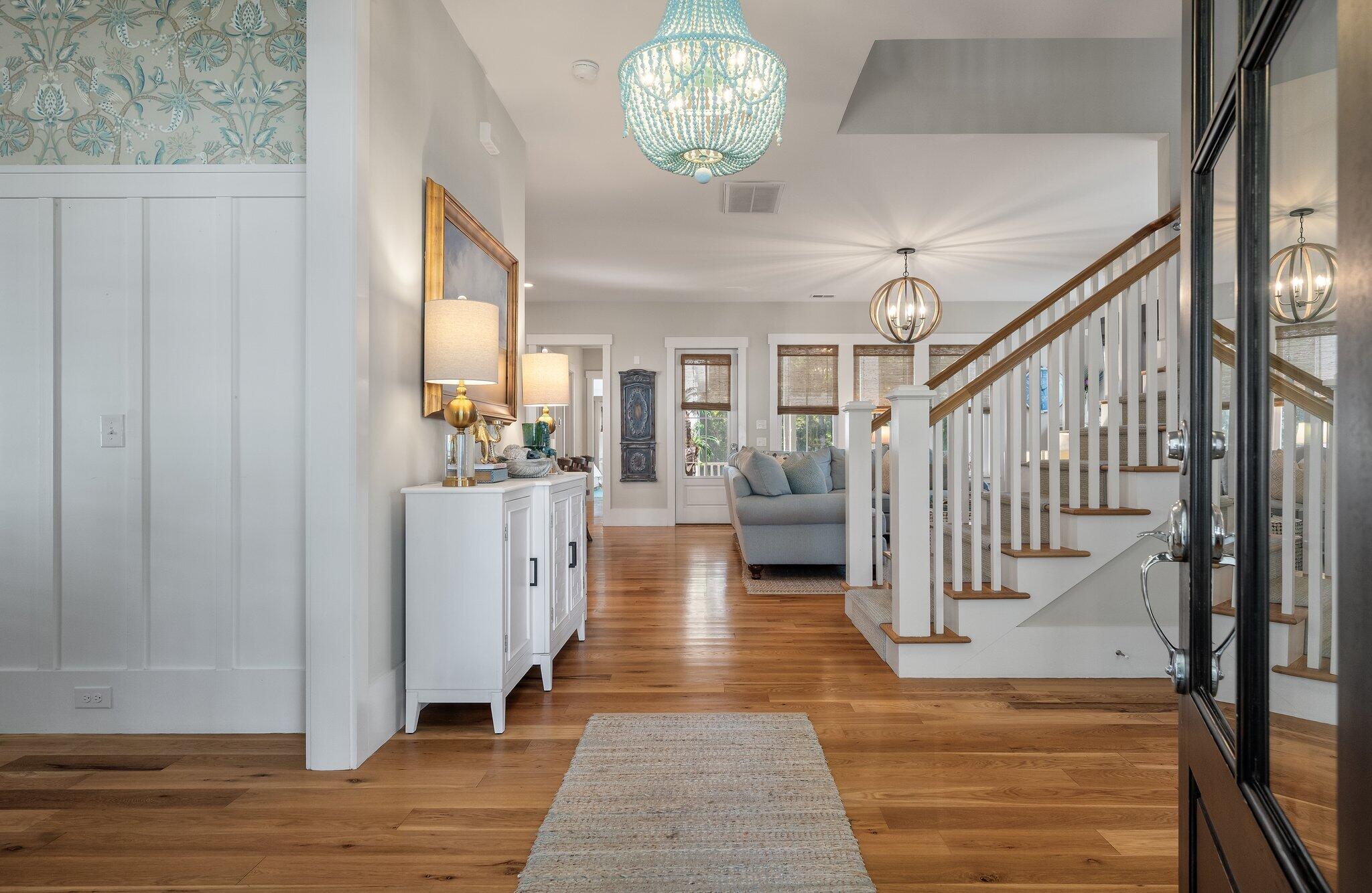 Entry hall with hardwood floors, a turquoise chandelier, and a staircase beside the living area.
