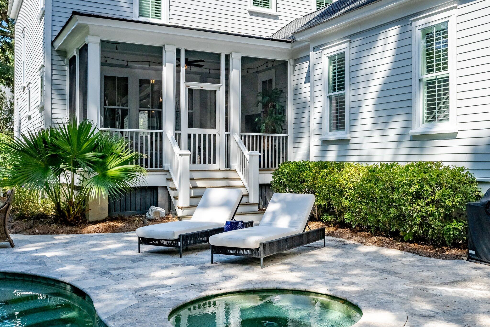 House backyard patio with screened porch, two white lounge chairs, and a curved pool with spa.