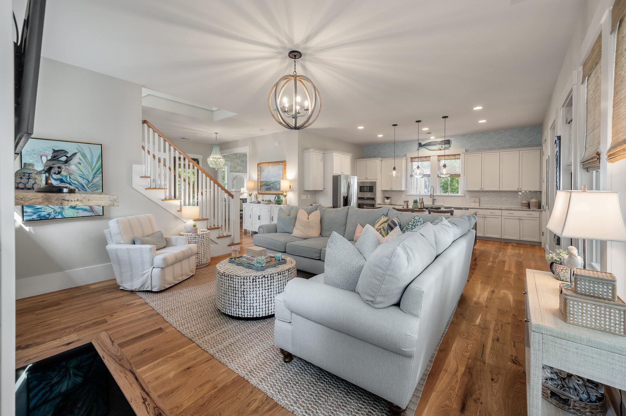 Open-plan living room and kitchen with a gray sectional, hardwood floors, and white cabinetry.