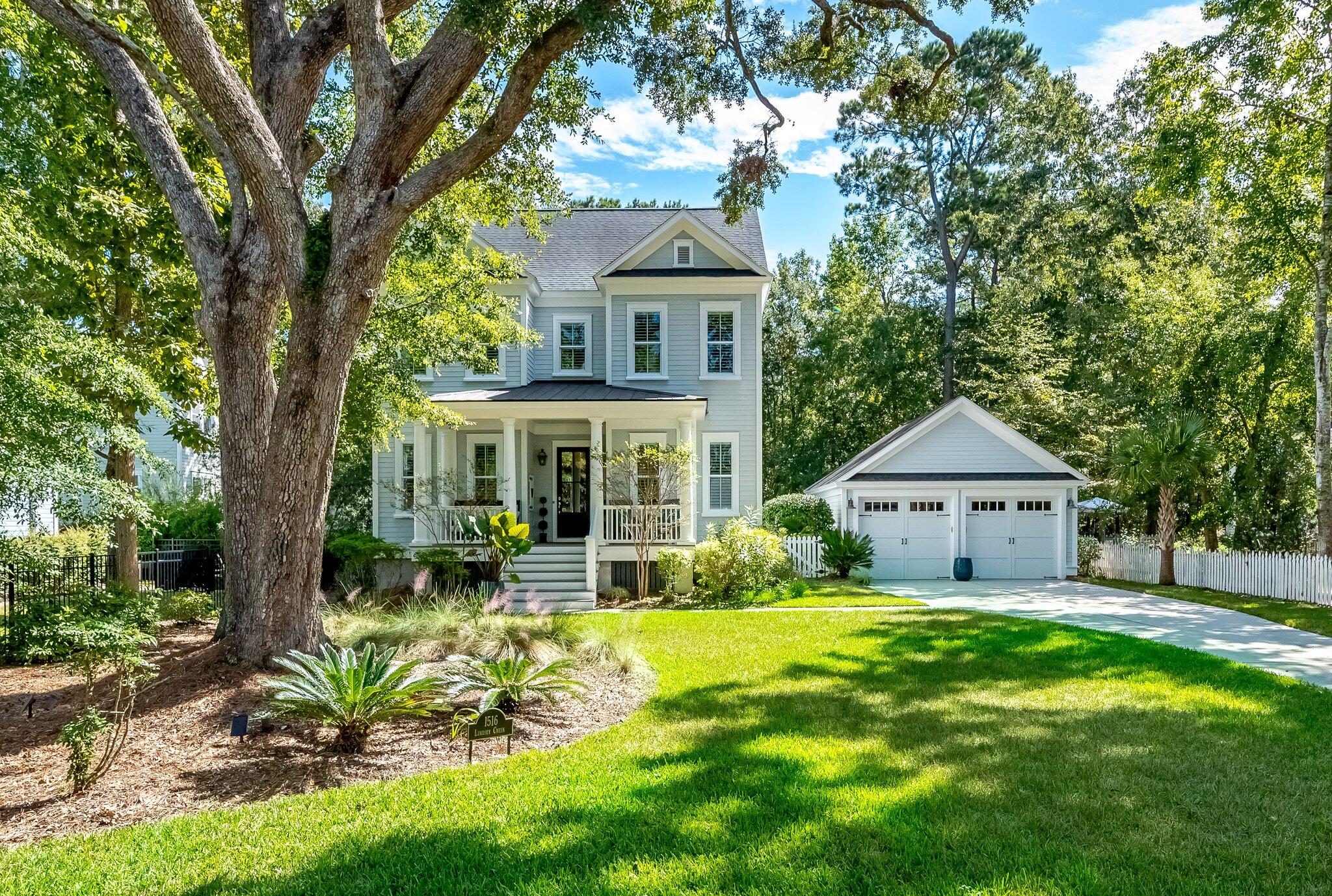 Two-story gray house with a covered porch, detached garage, and mature oak trees.