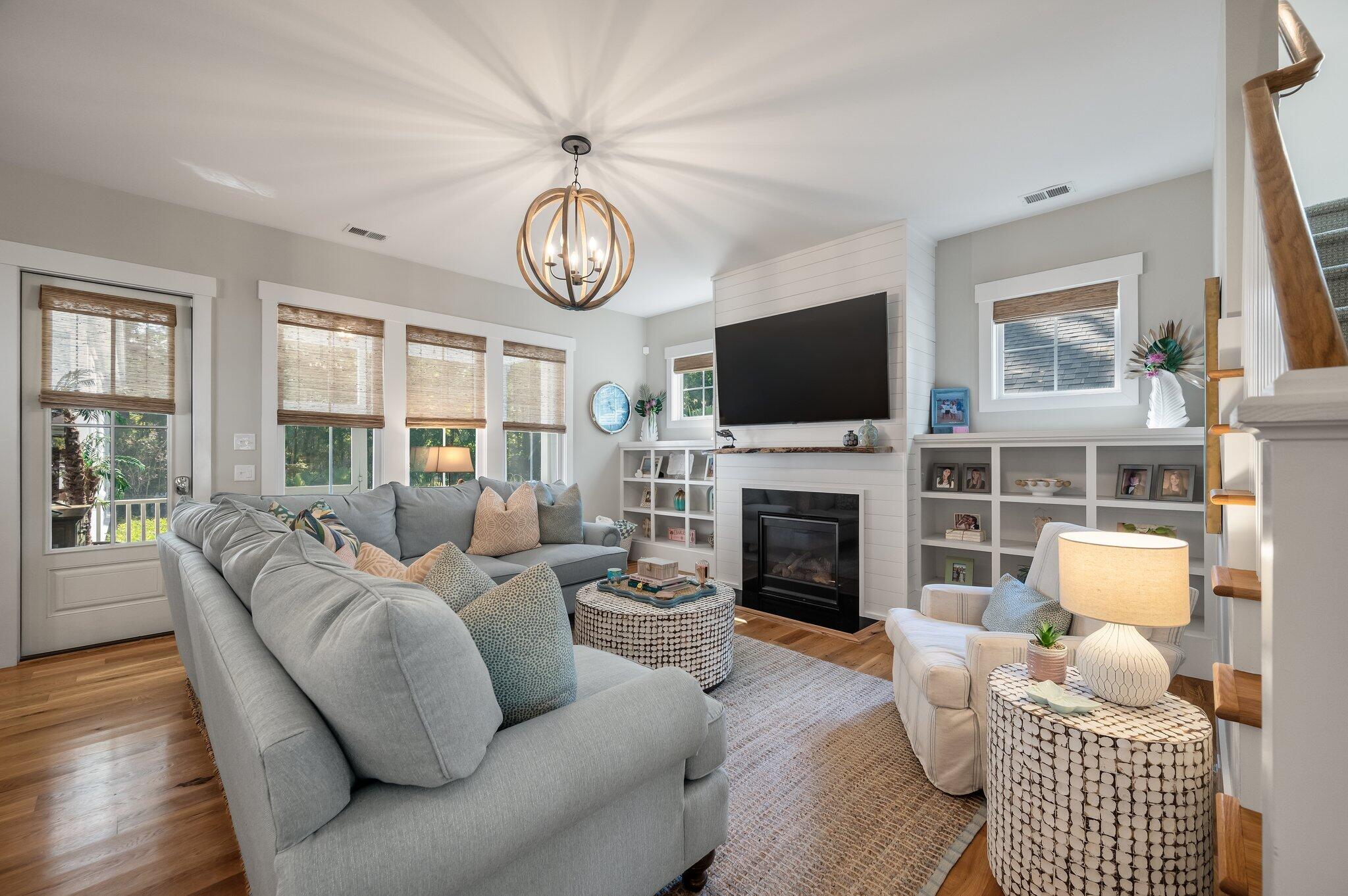 Living room with a gray sectional, shiplap fireplace, built-in shelves, and large windows.