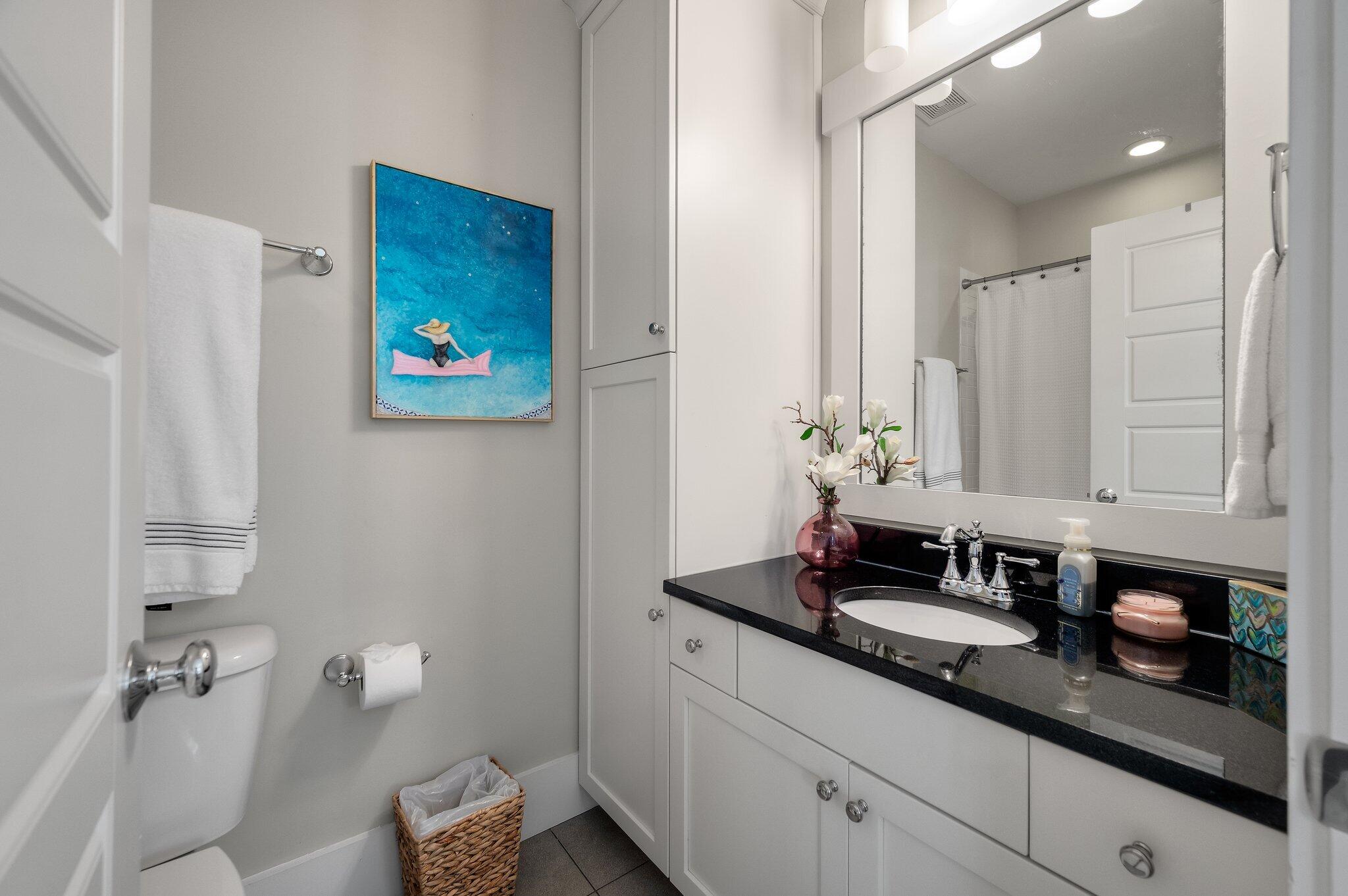 Bathroom with white cabinetry and black countertop, large mirror, and blue artwork above the towel bar.