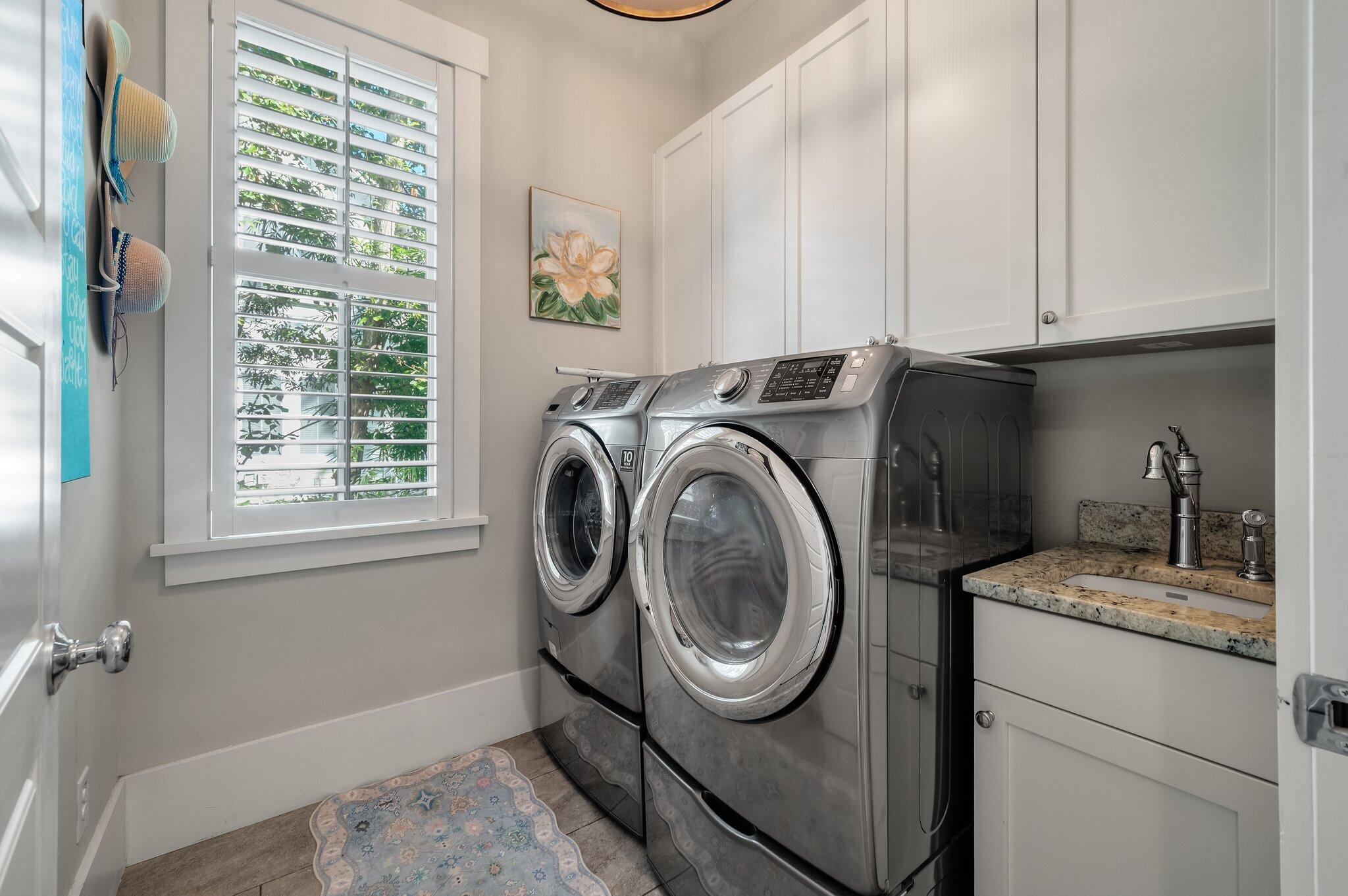 Laundry room with front-loading washer and dryer, granite utility sink, and plantation-shuttered window.