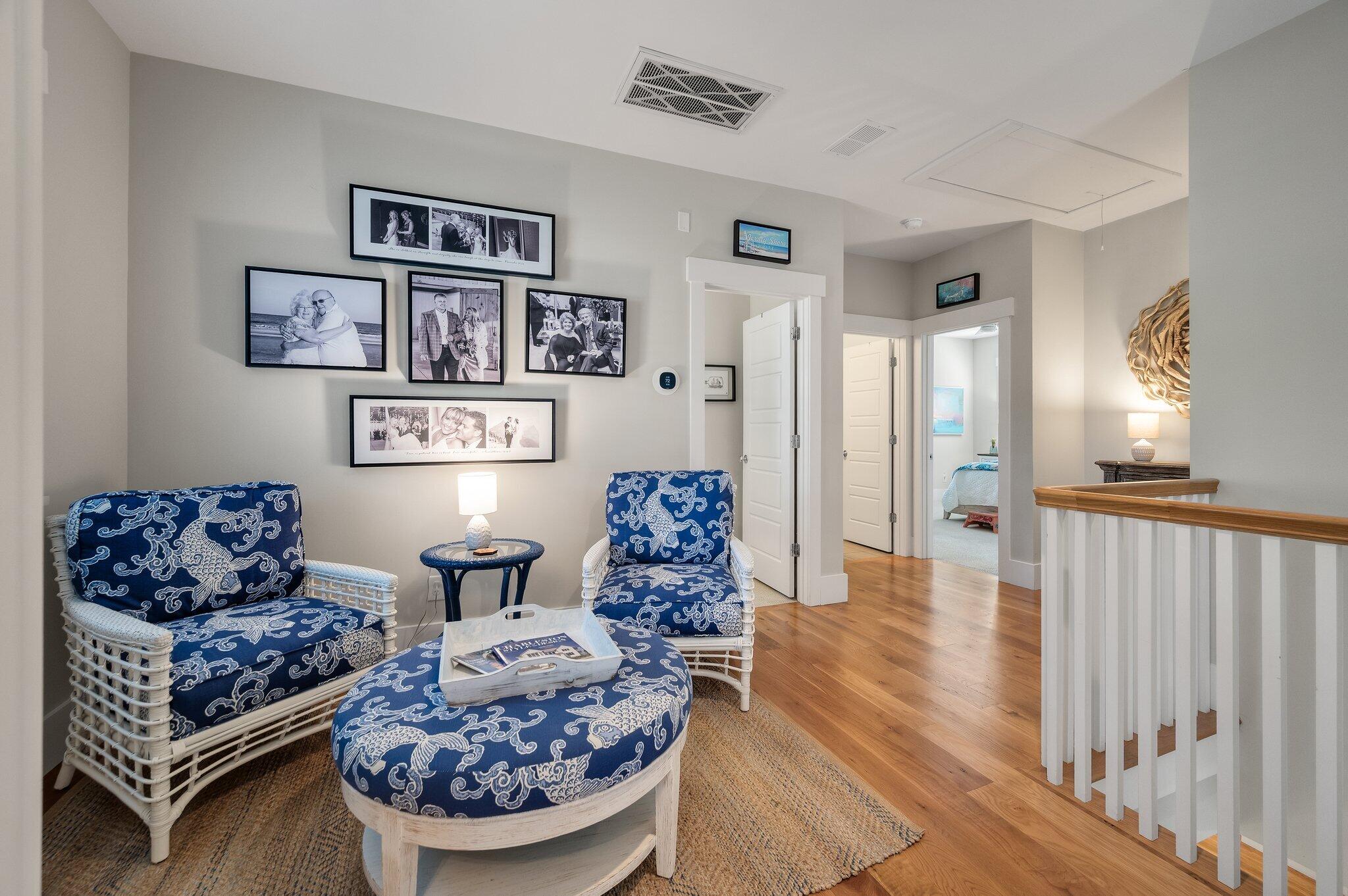 Upstairs sitting area with blue patterned wicker seating, framed family photos, and a white stair railing.