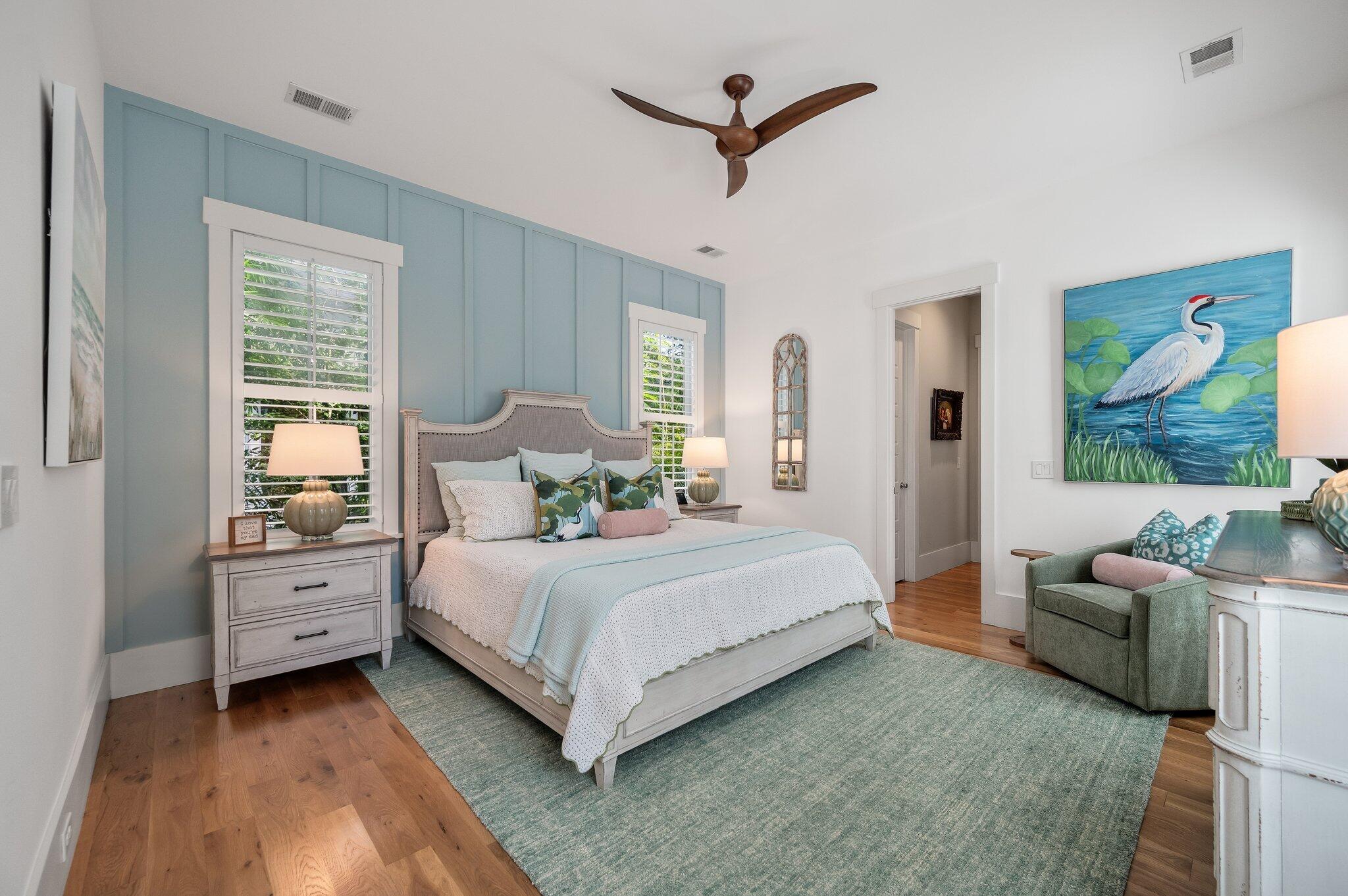 Bedroom with a blue paneled accent wall, shuttered windows, and a painted egret above a green armchair.