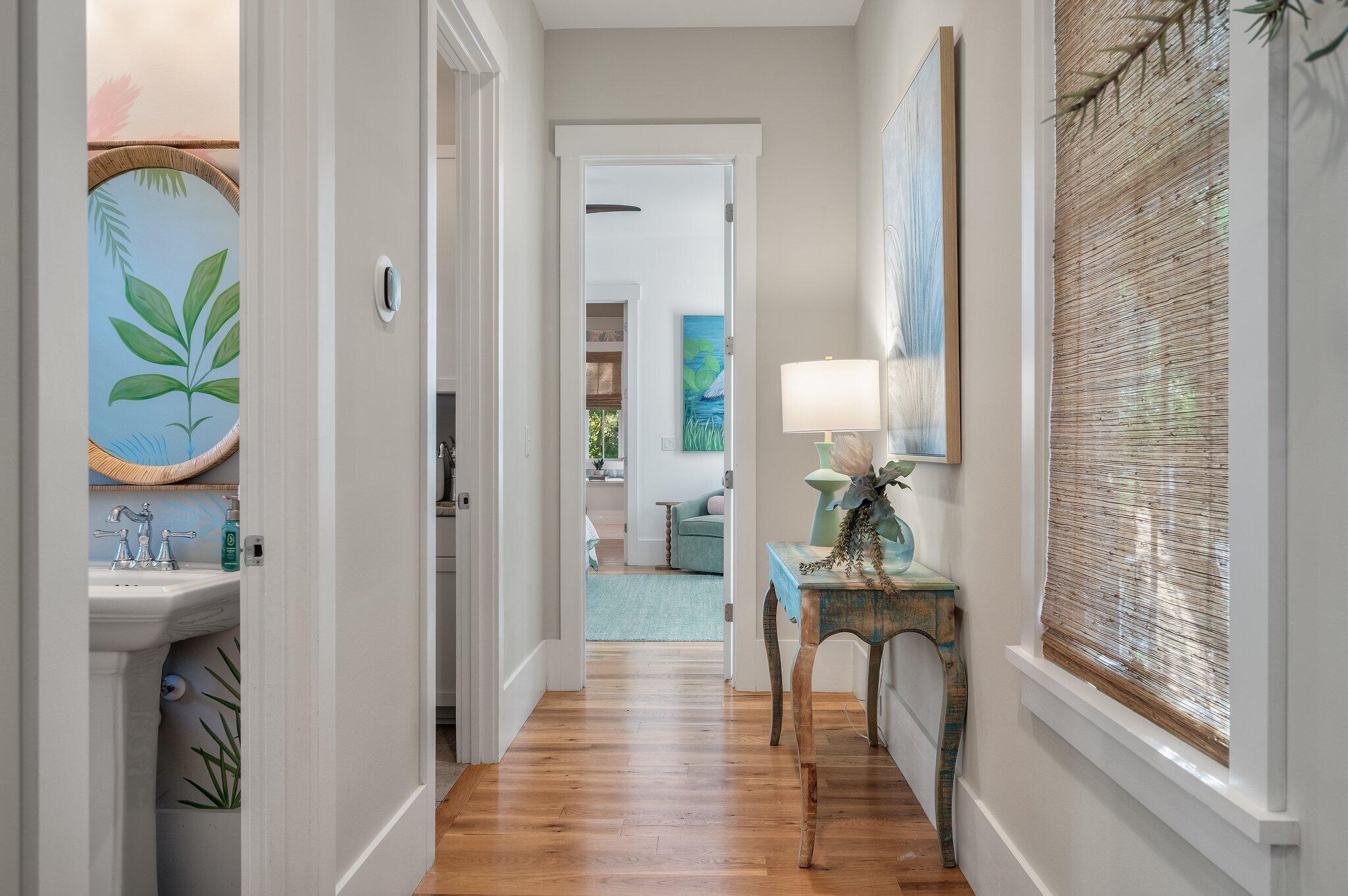 Furnished hallway with hardwood floors, a rustic console table, and a bathroom sink visible through an open doorway.