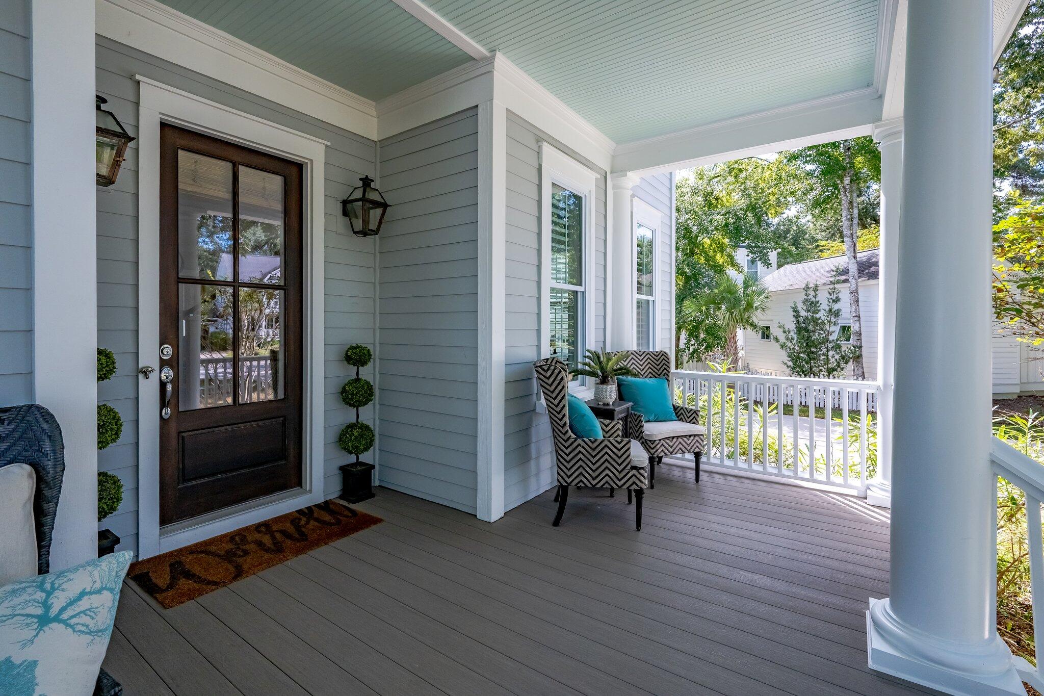 Covered front porch with a dark entry door, white columns, and patterned chairs with turquoise cushions.