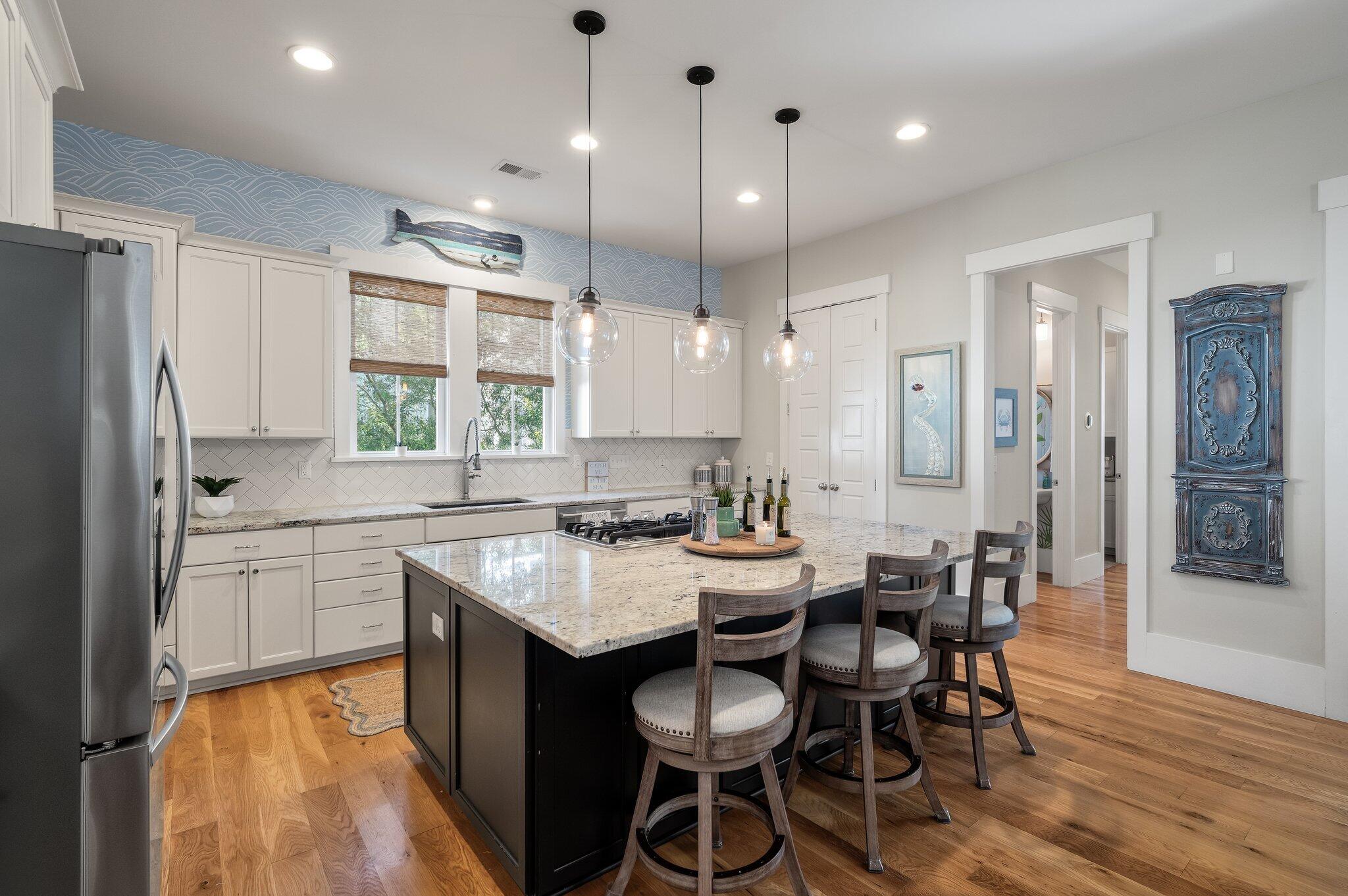 Kitchen with a large island, four stools, white cabinets, and blue wave-pattern wallpaper.