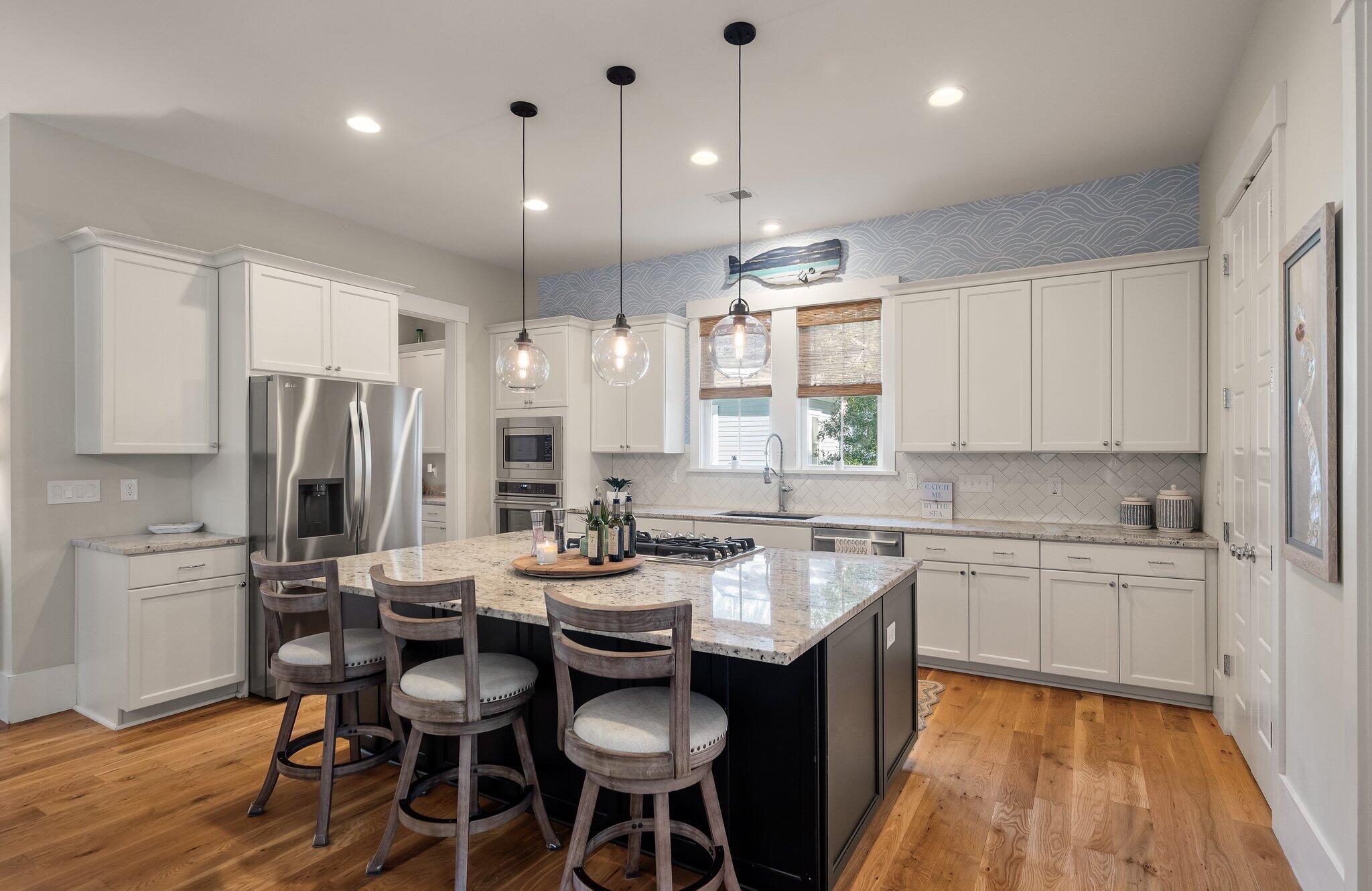 Kitchen with a large granite island, white cabinets, pendant lights, and hardwood floors.