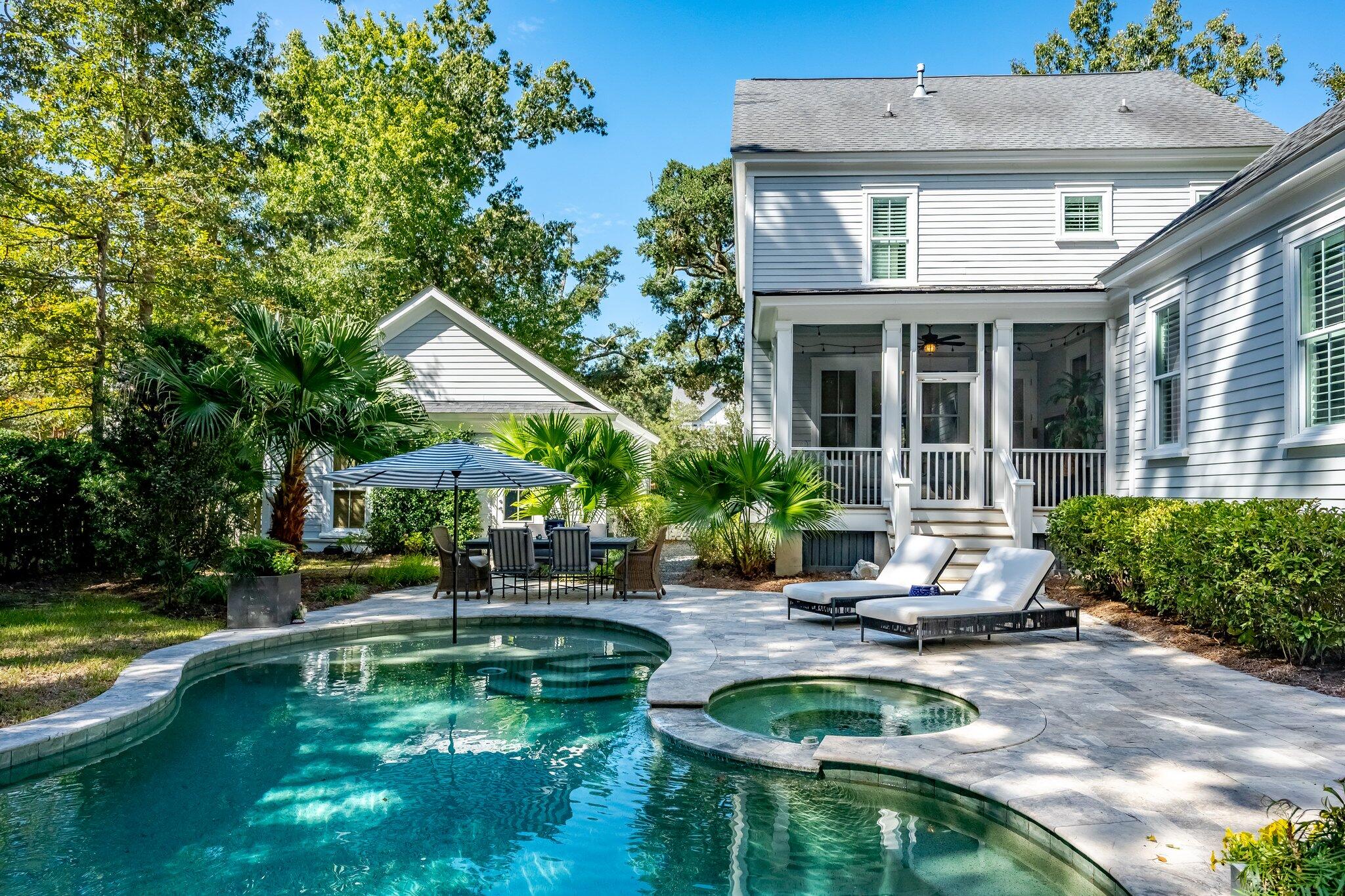 Backyard swimming pool and spa beside a gray home, with a covered porch and furnished stone patio.