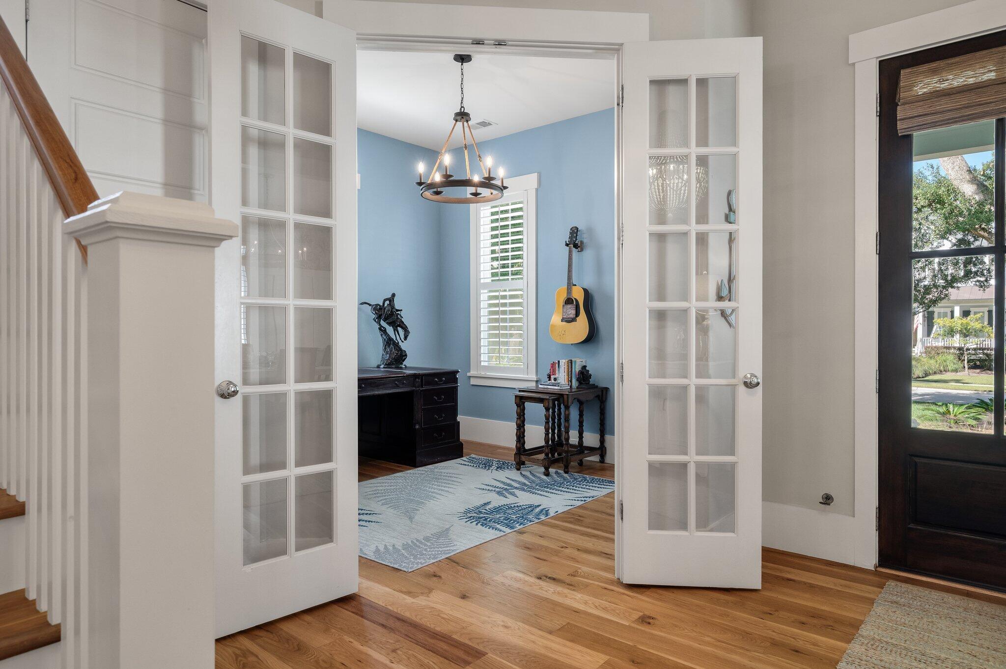 Blue home office with a hanging guitar, chandelier, and open glass-paneled doors.