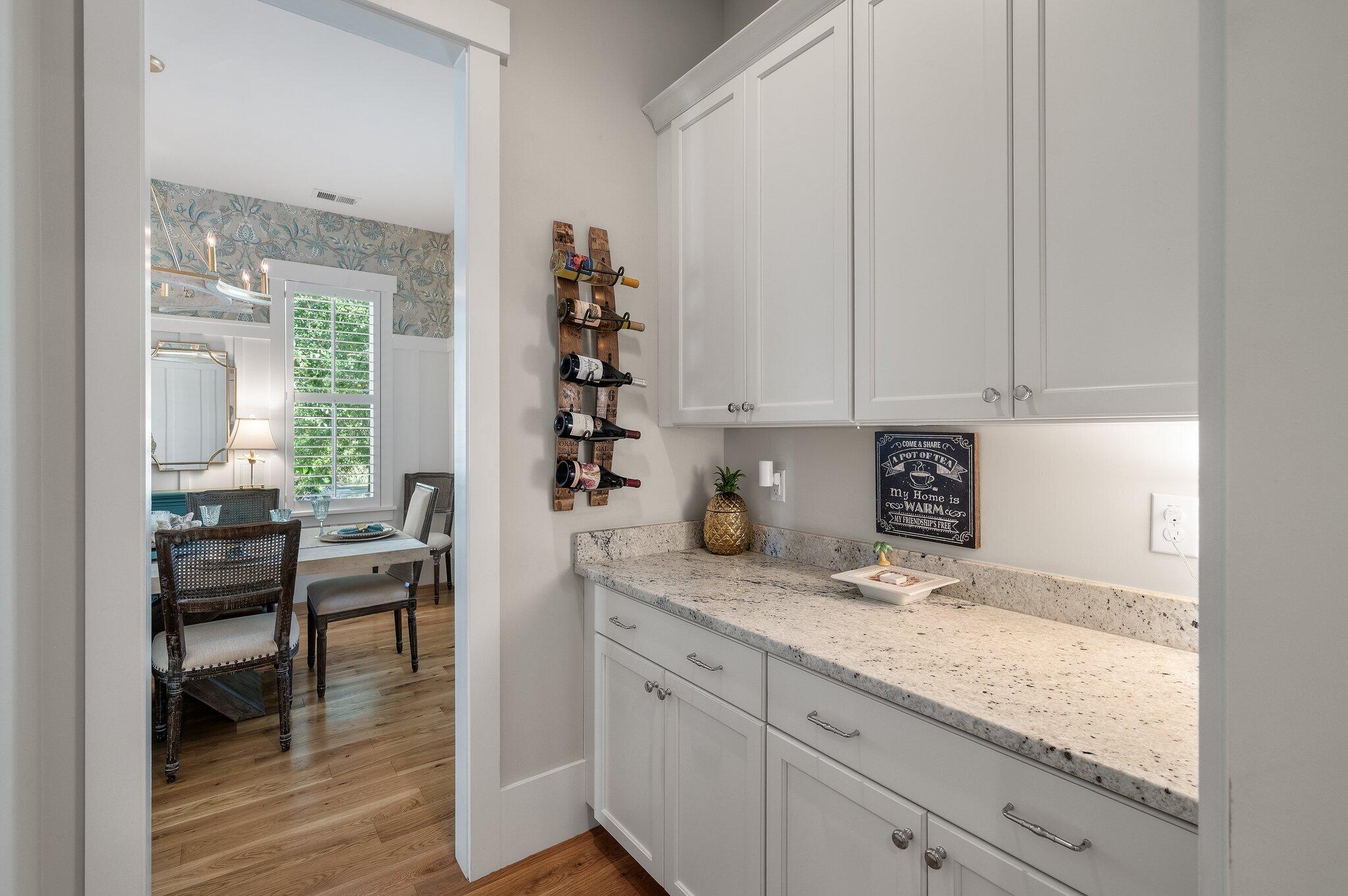 Butler’s pantry with white cabinets, granite counters, and a wall-mounted wine rack beside the dining area.