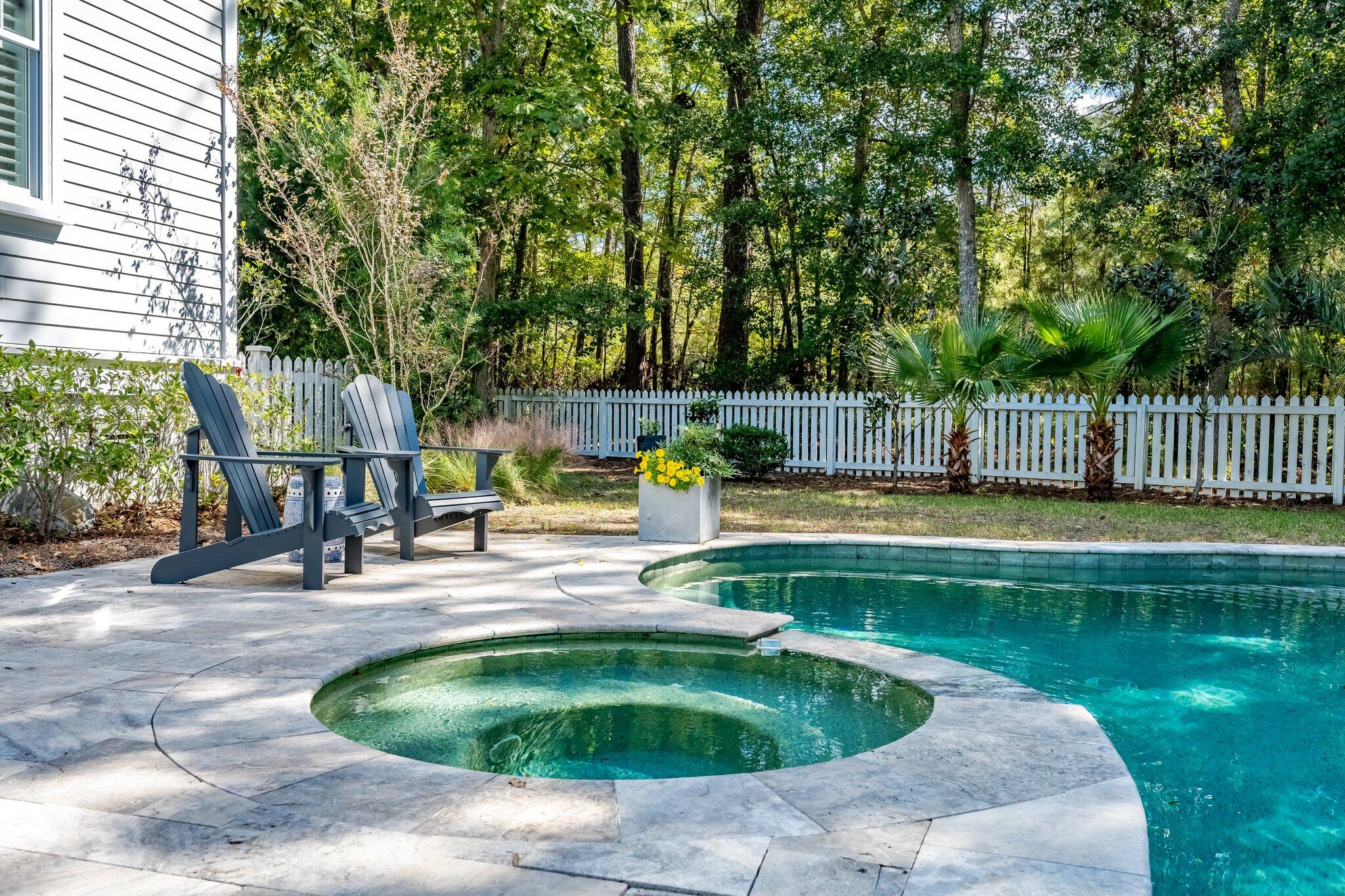 Backyard pool and circular spa with stone patio, Adirondack chairs, and a wooded fenced yard.