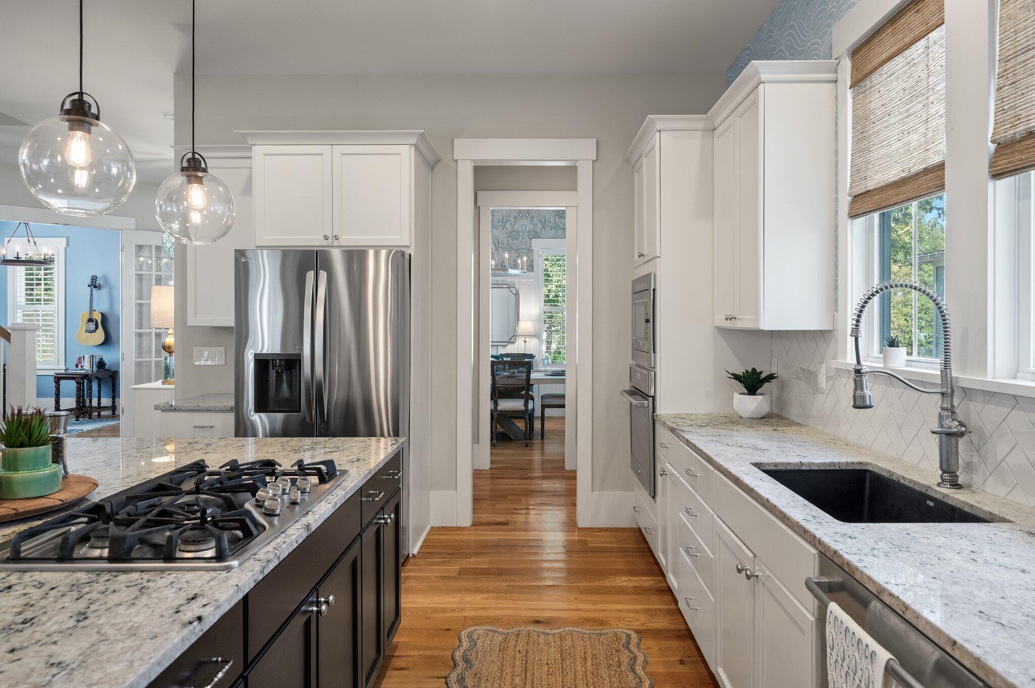 Kitchen with white cabinets, granite counters, dark gas-cooktop island, and stainless steel appliances.