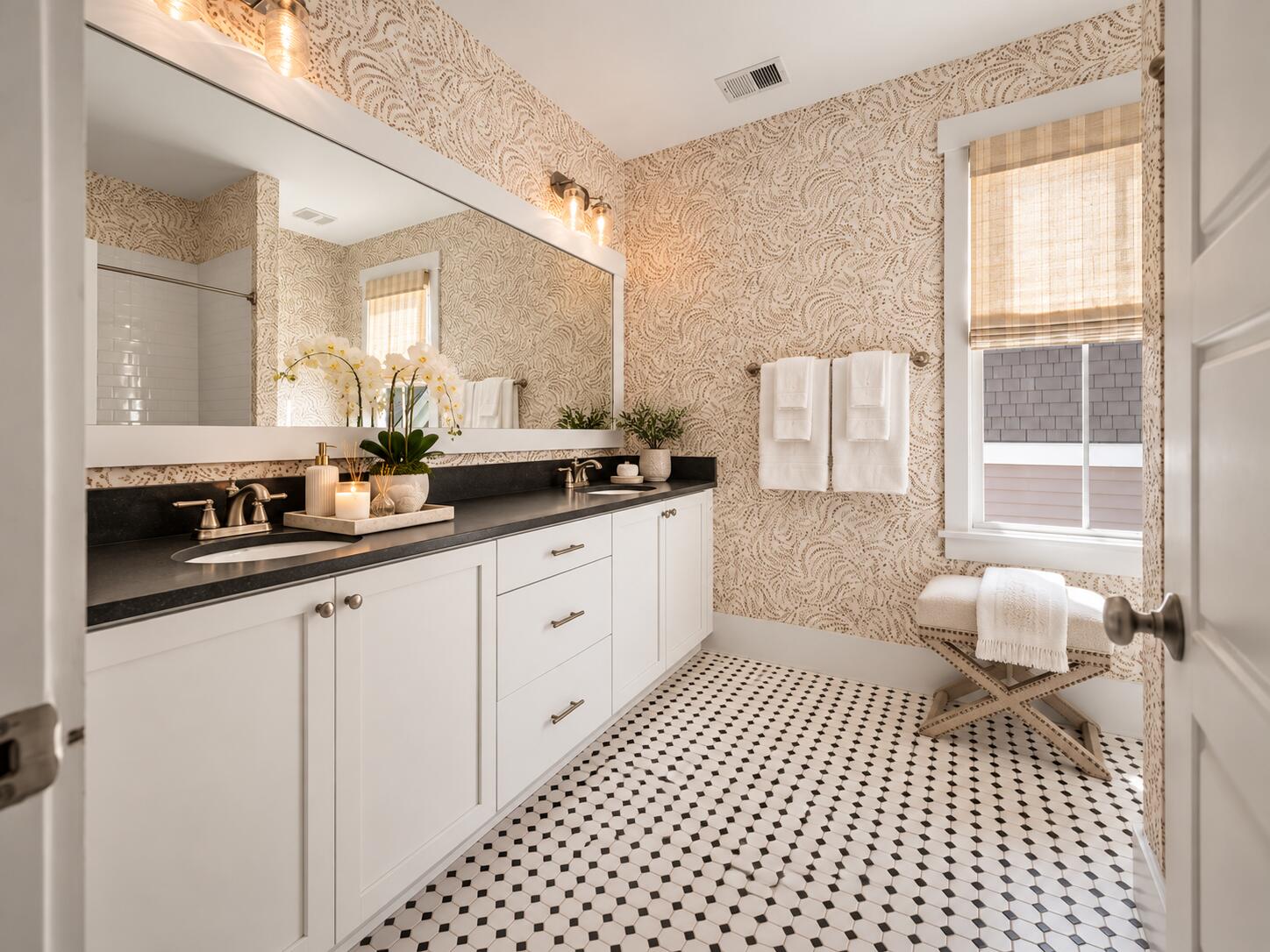 Bathroom with a long double vanity, patterned wallpaper, and black-and-white tile floor.
