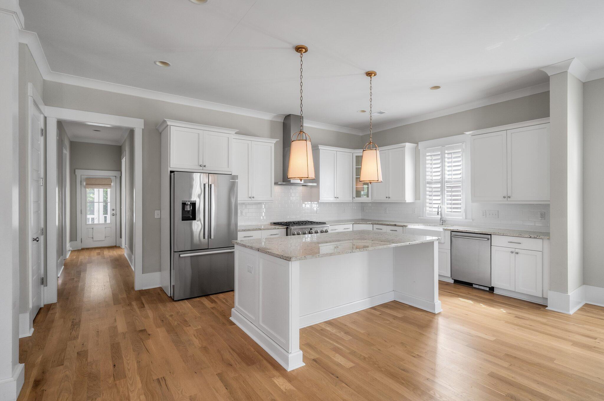 Bright kitchen with a large island, white cabinetry, stainless steel appliances, and hardwood floors.