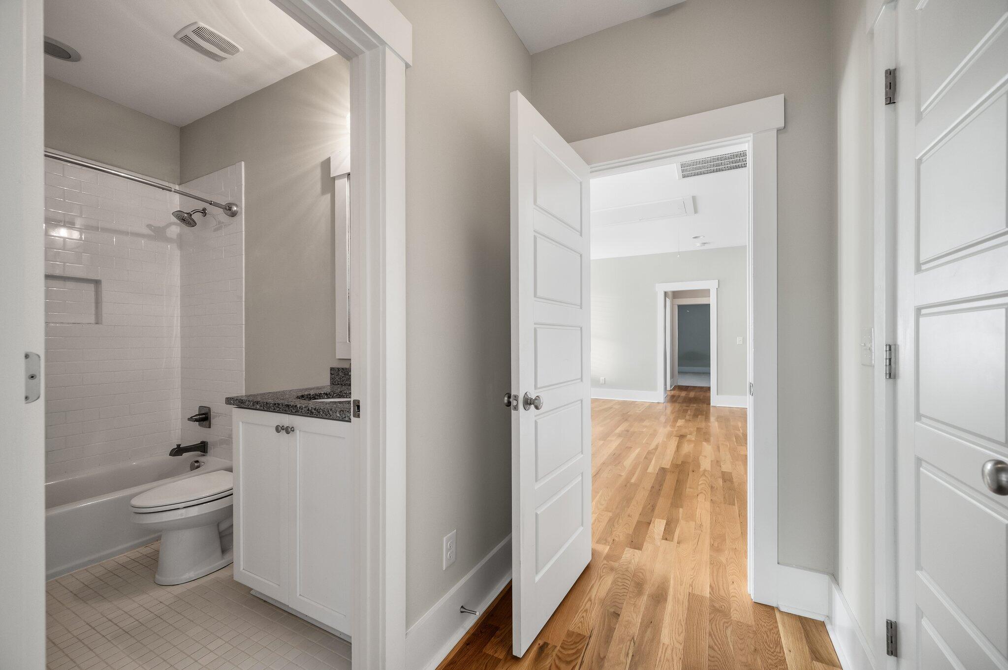 Bathroom with a tiled tub and granite vanity opening onto a hardwood-floored hallway.