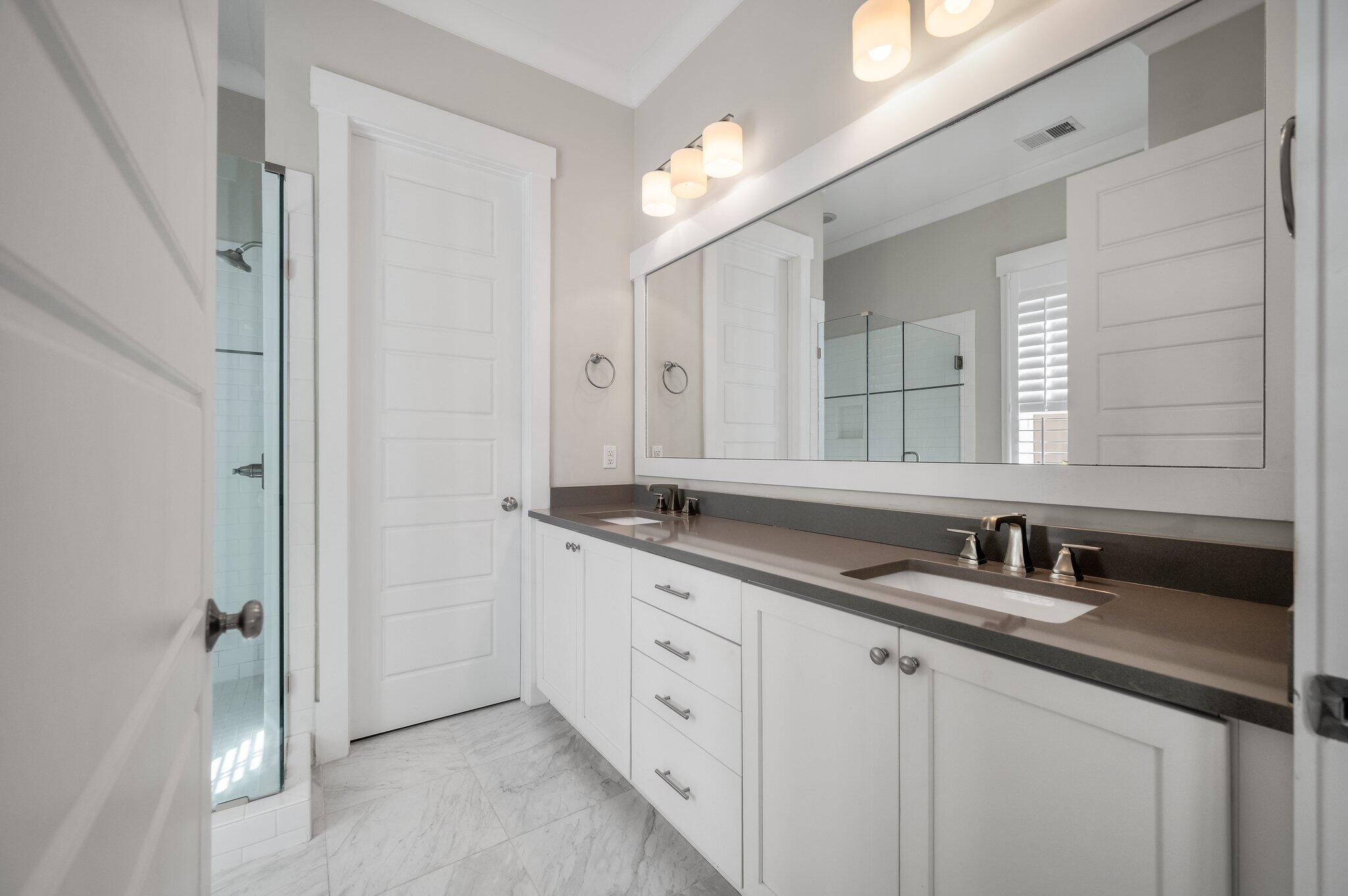 Bathroom with a long double-sink vanity, oversized mirror, and glass-enclosed shower.