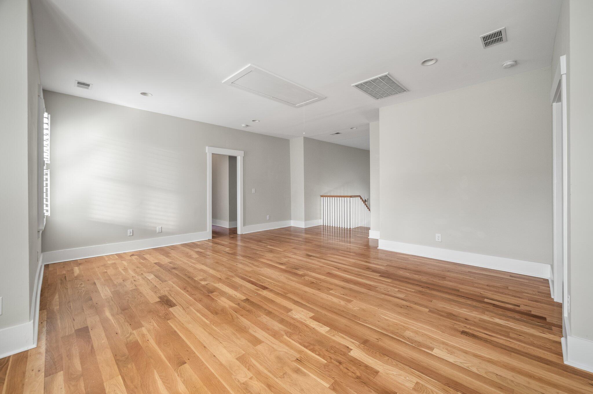 Vacant living area with hardwood floors, gray walls, and a staircase railing.