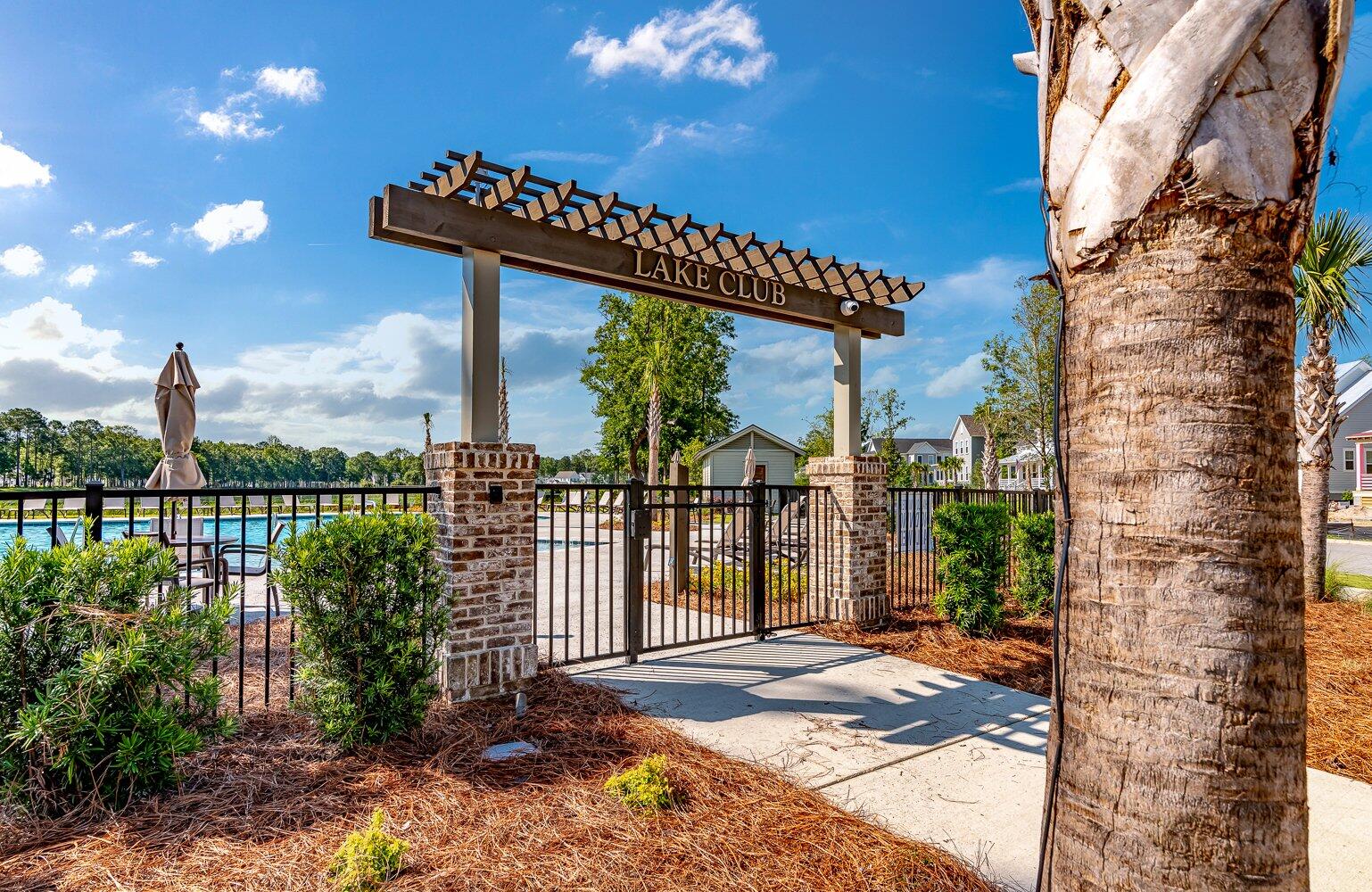 Lake Club pool entrance with a pergola gate, palm trees, and swimming pool.