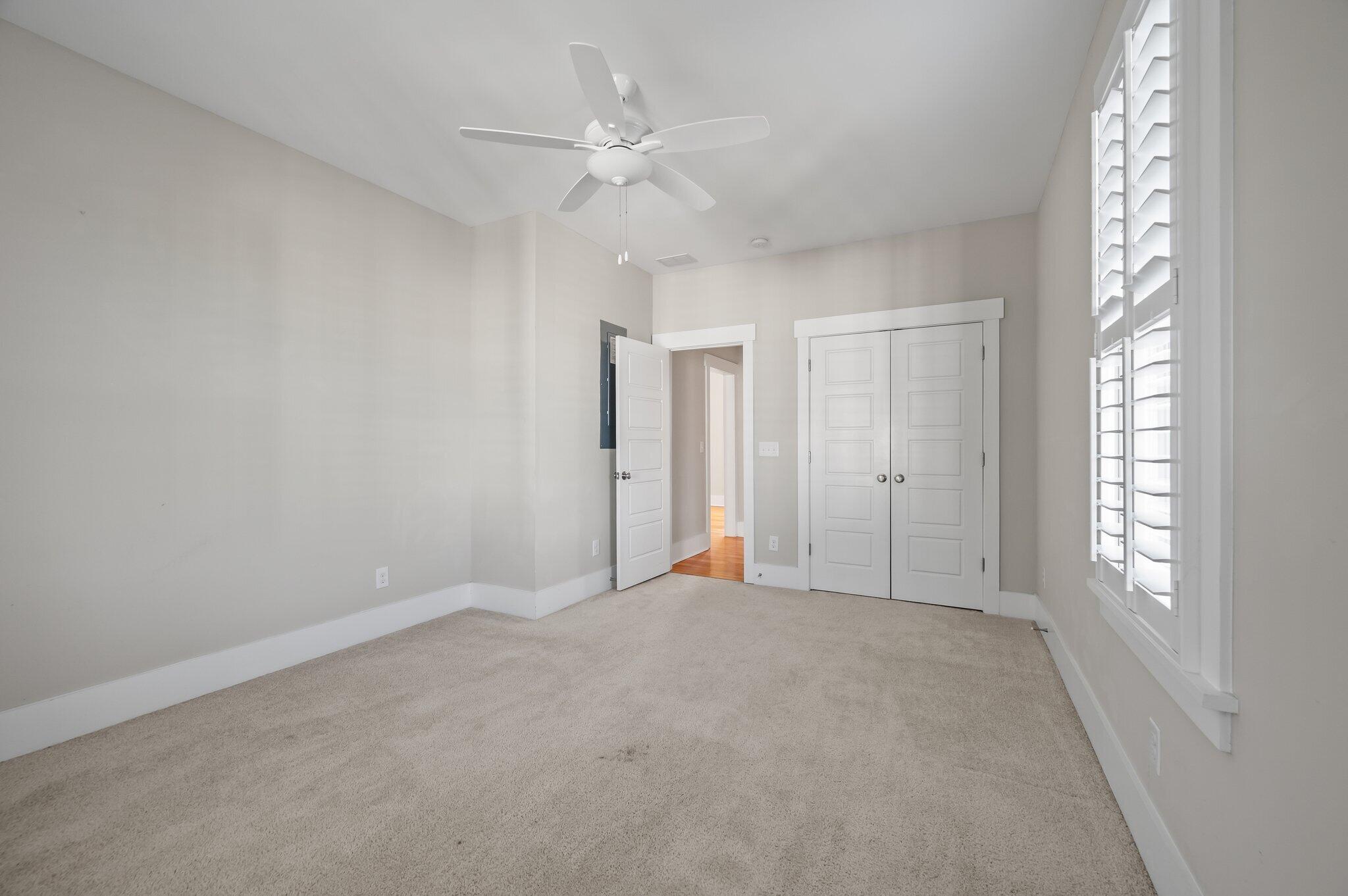 Vacant carpeted bedroom with a ceiling fan, plantation shutters, and double closet doors.