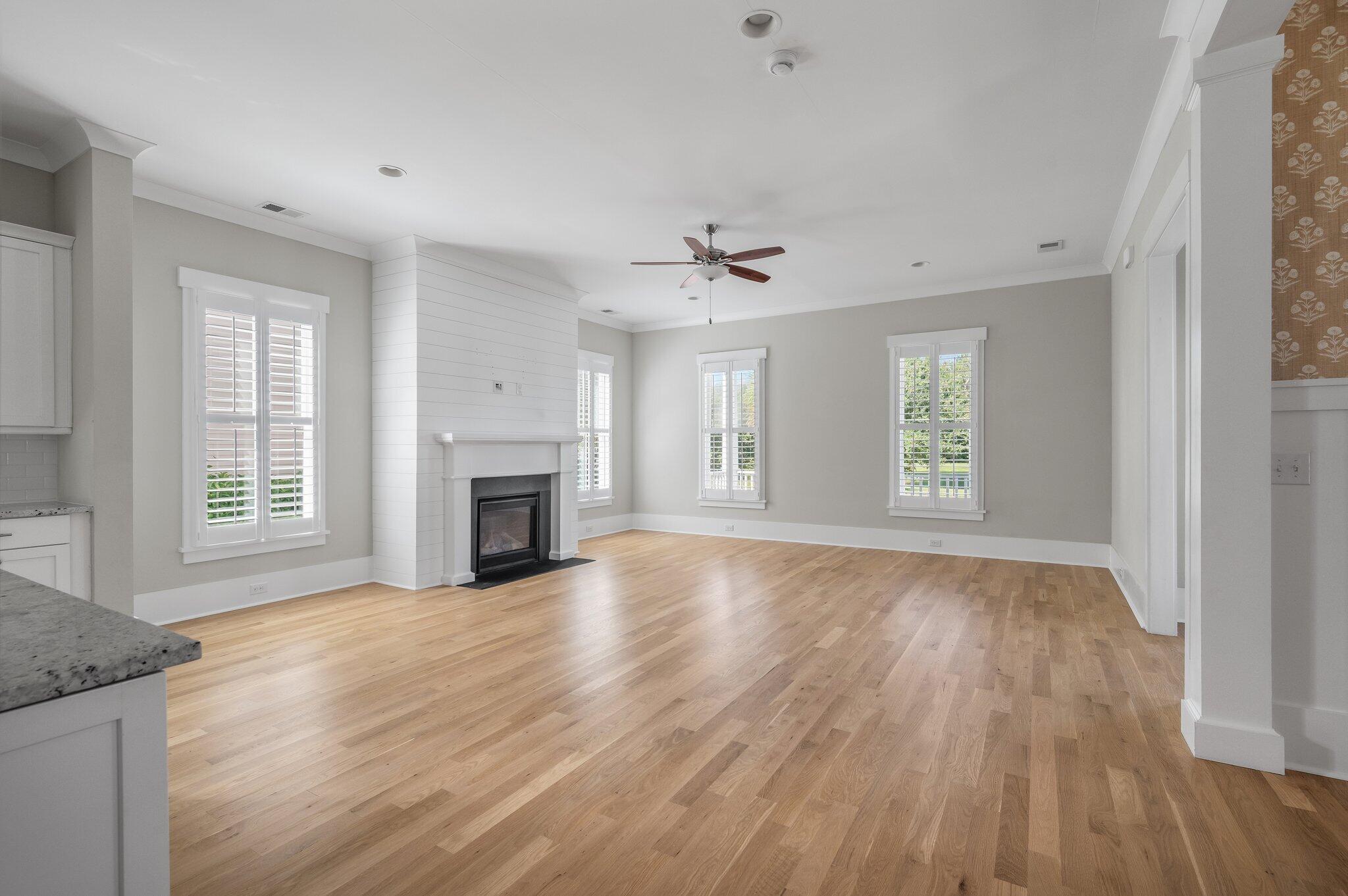 Open living room with hardwood floors, a white fireplace, and plantation-shuttered windows.