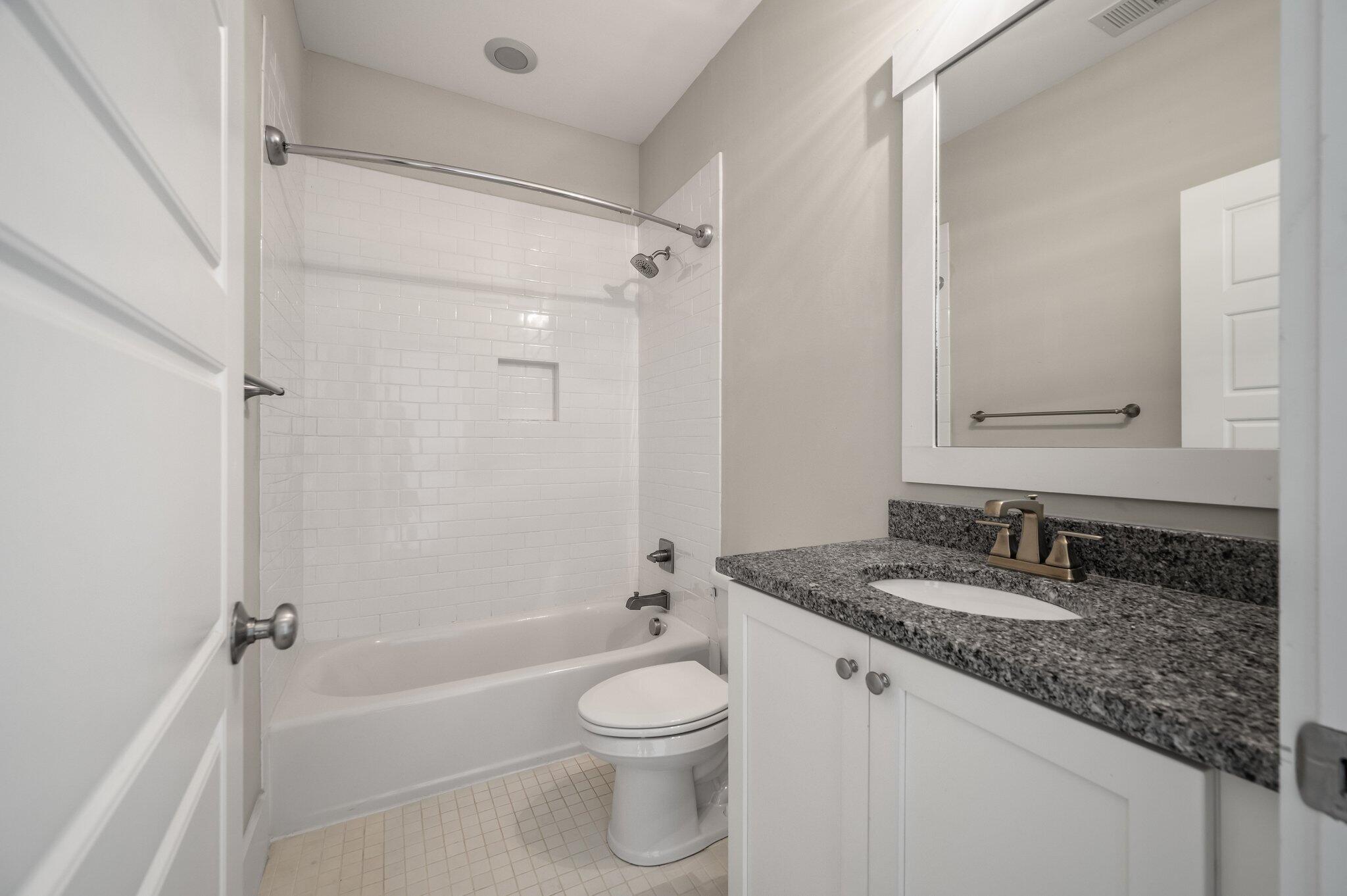Bathroom with a white tile tub and shower beside a granite vanity.
