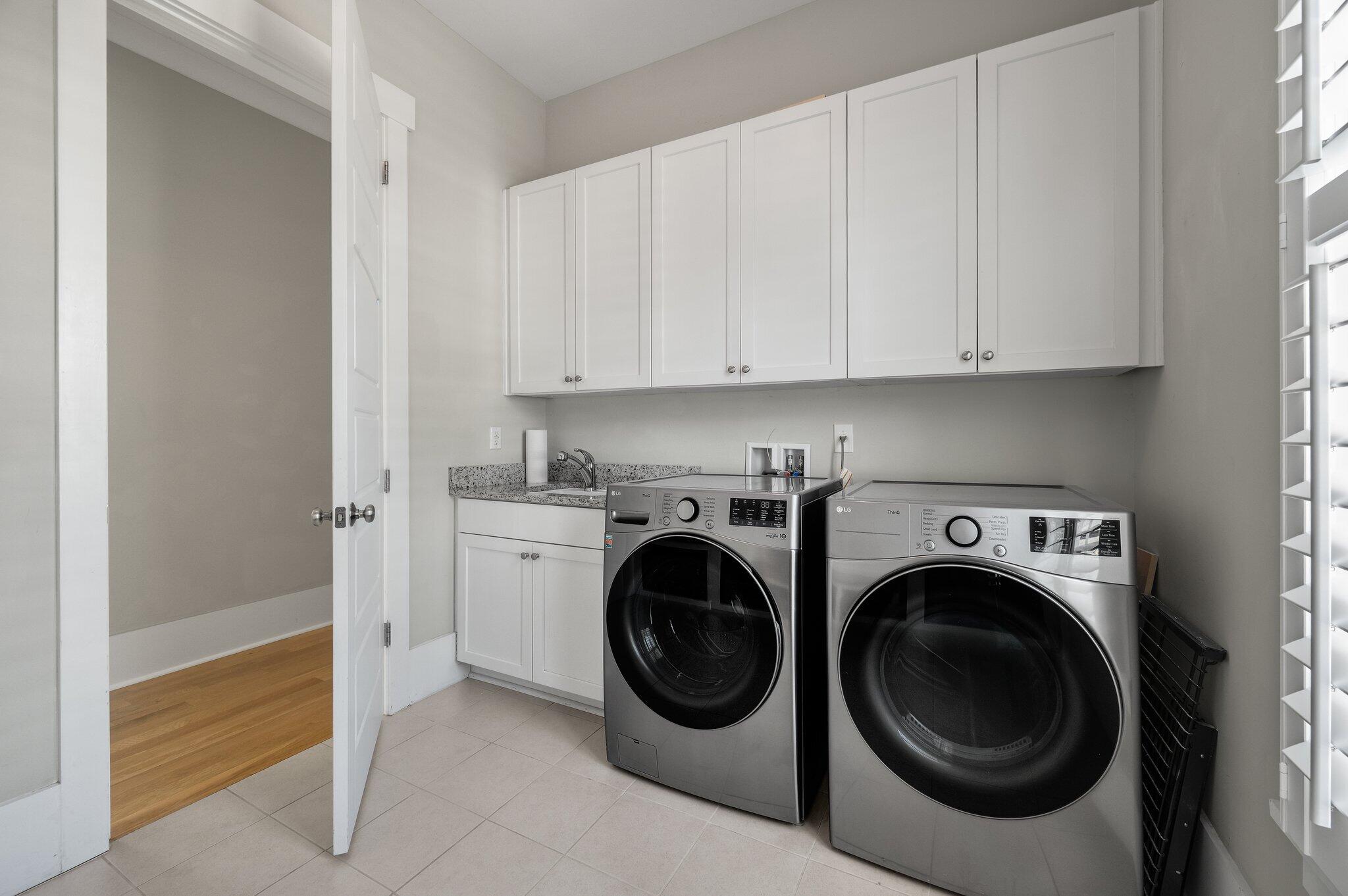Laundry room with front-loading washer and dryer, white cabinets, and a utility sink.