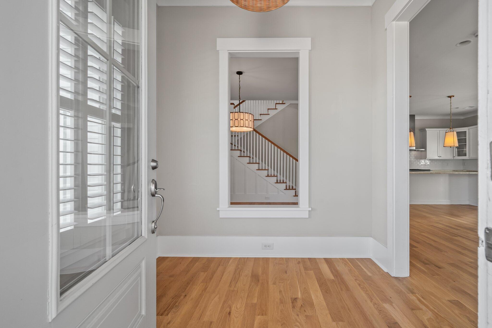 Entry foyer with hardwood floors, a shuttered glass door, and a staircase beyond.