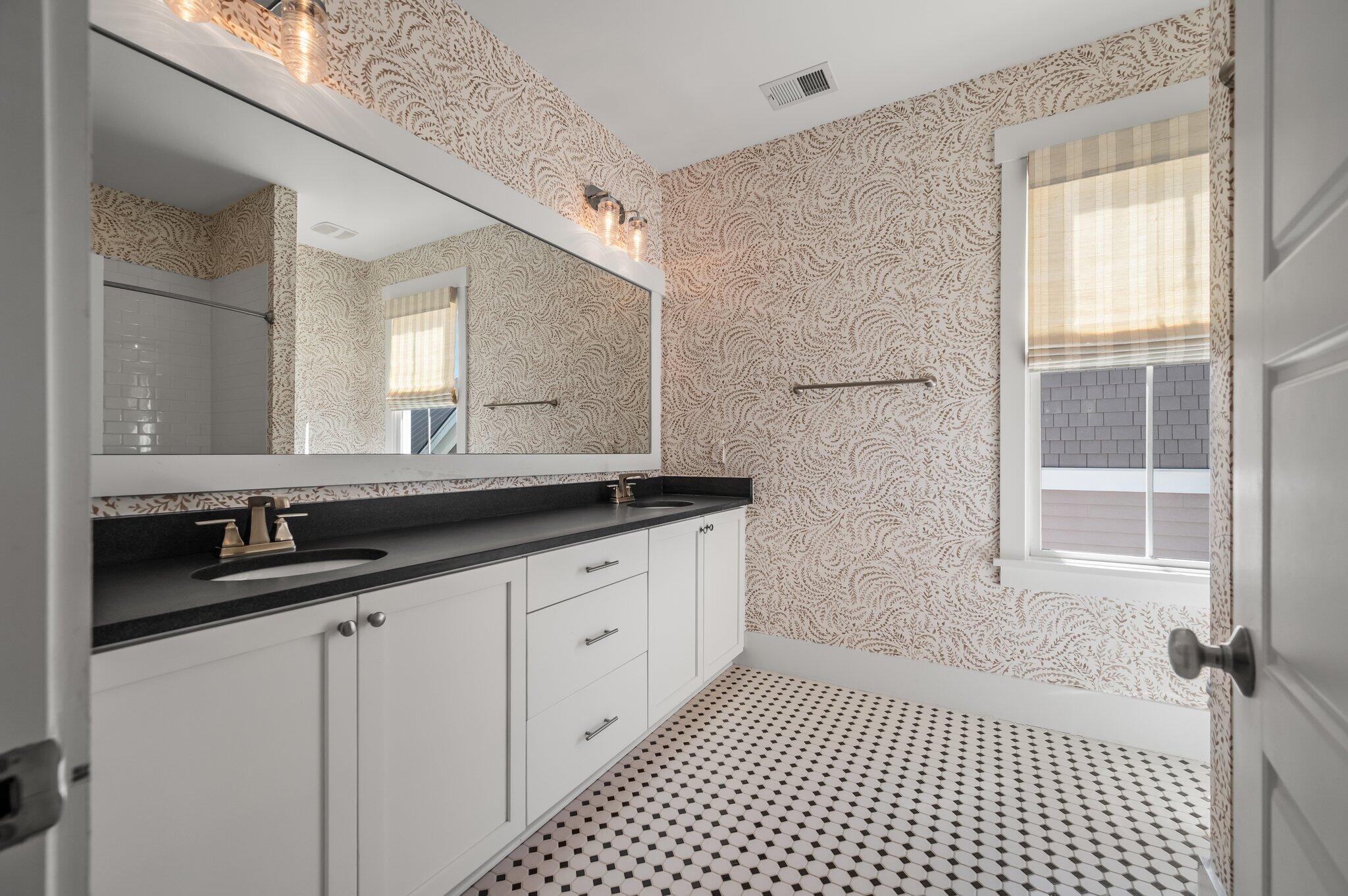 Bathroom with a double vanity, patterned wallpaper, and black-and-white tile floor.