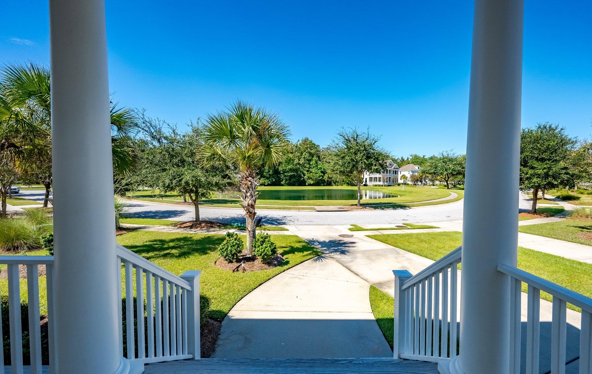 Porch view over a landscaped pond, curved street, and palm trees.