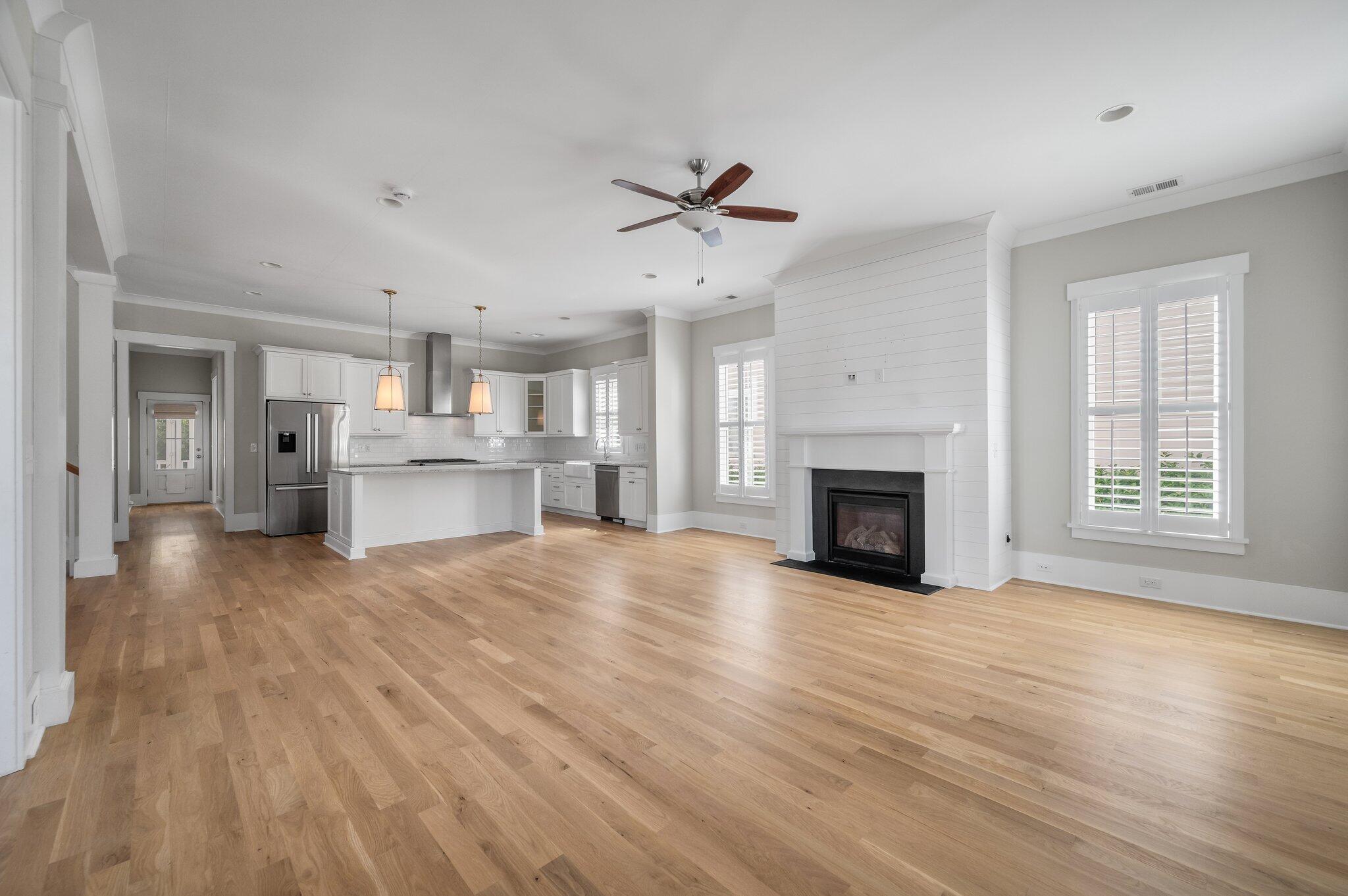 Open living room and kitchen with a shiplap fireplace, white cabinetry, and hardwood floors.