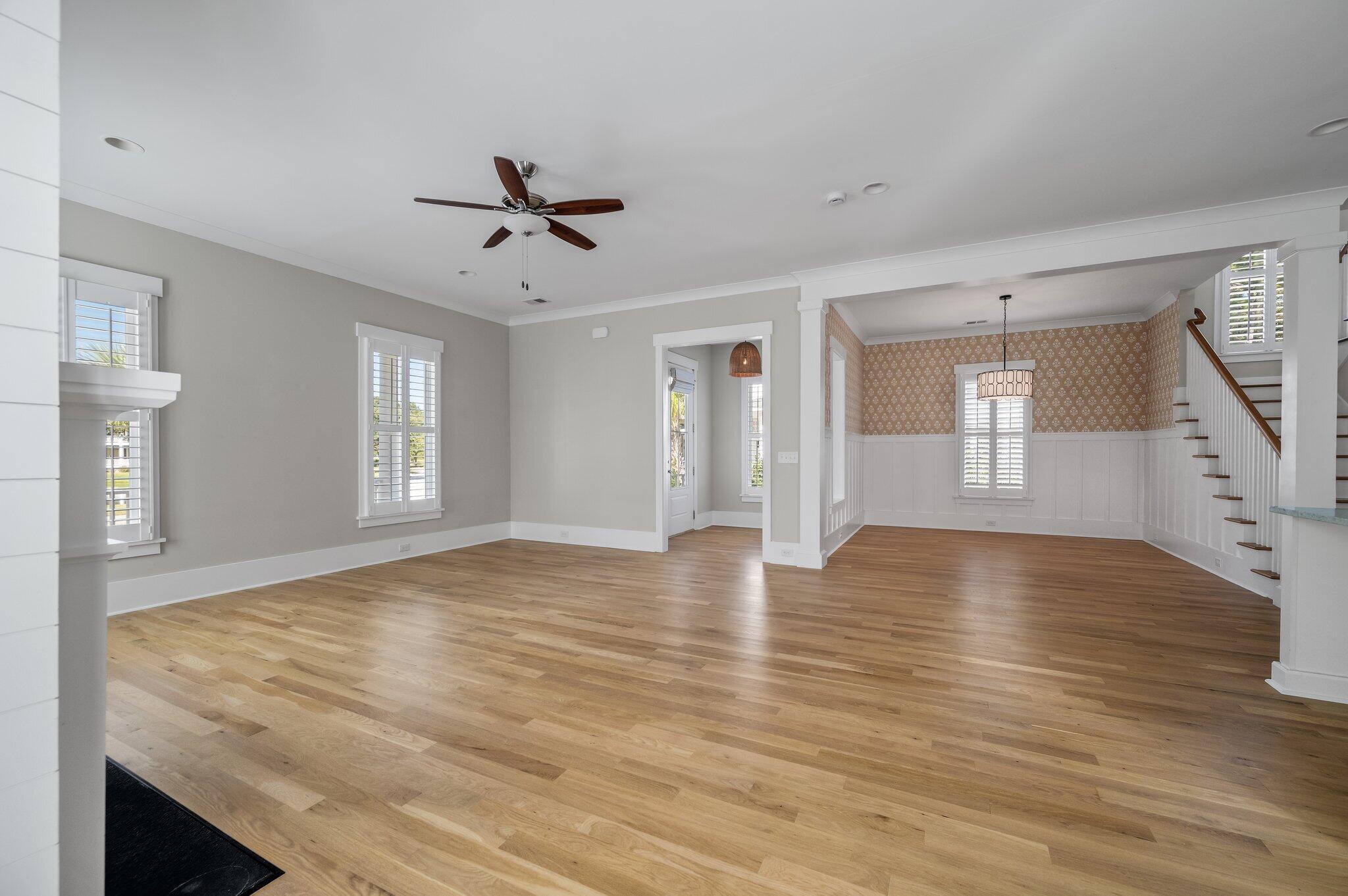 Empty living room with hardwood floors, plantation shutters, and an adjoining wallpapered dining area.
