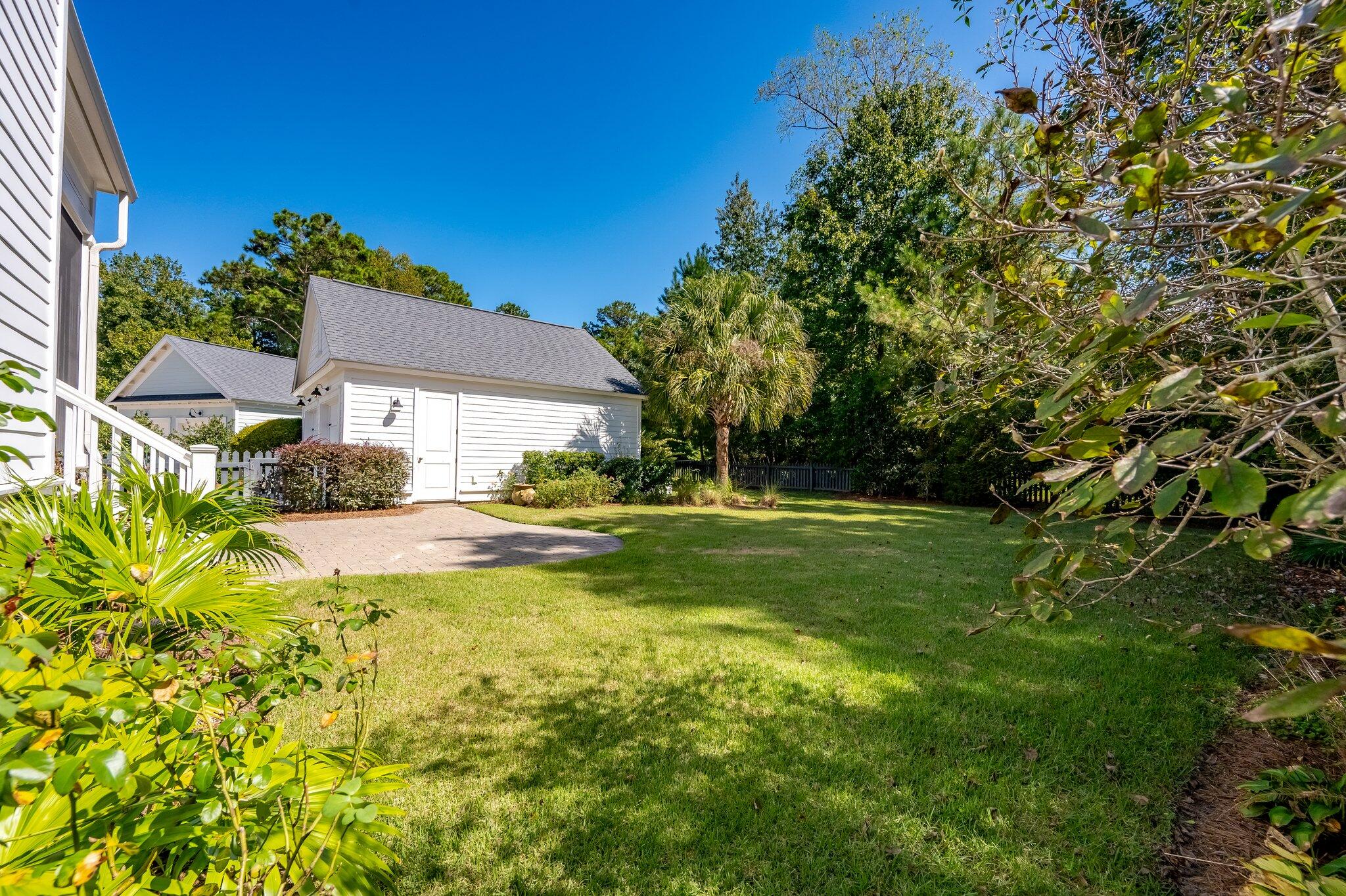 Backyard lawn and brick patio beside a white detached garage, surrounded by mature trees and landscaping.