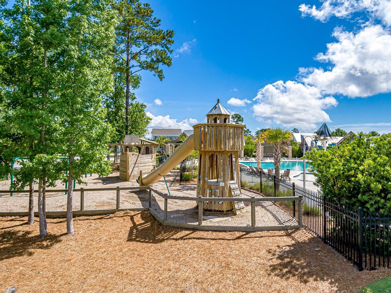 Community playground with a wooden tower and slide beside a swimming pool.