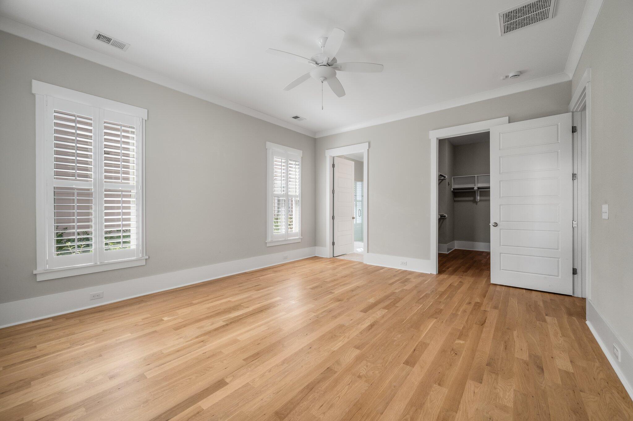 Empty bedroom with hardwood floors, plantation shutters, a ceiling fan, and an open closet.