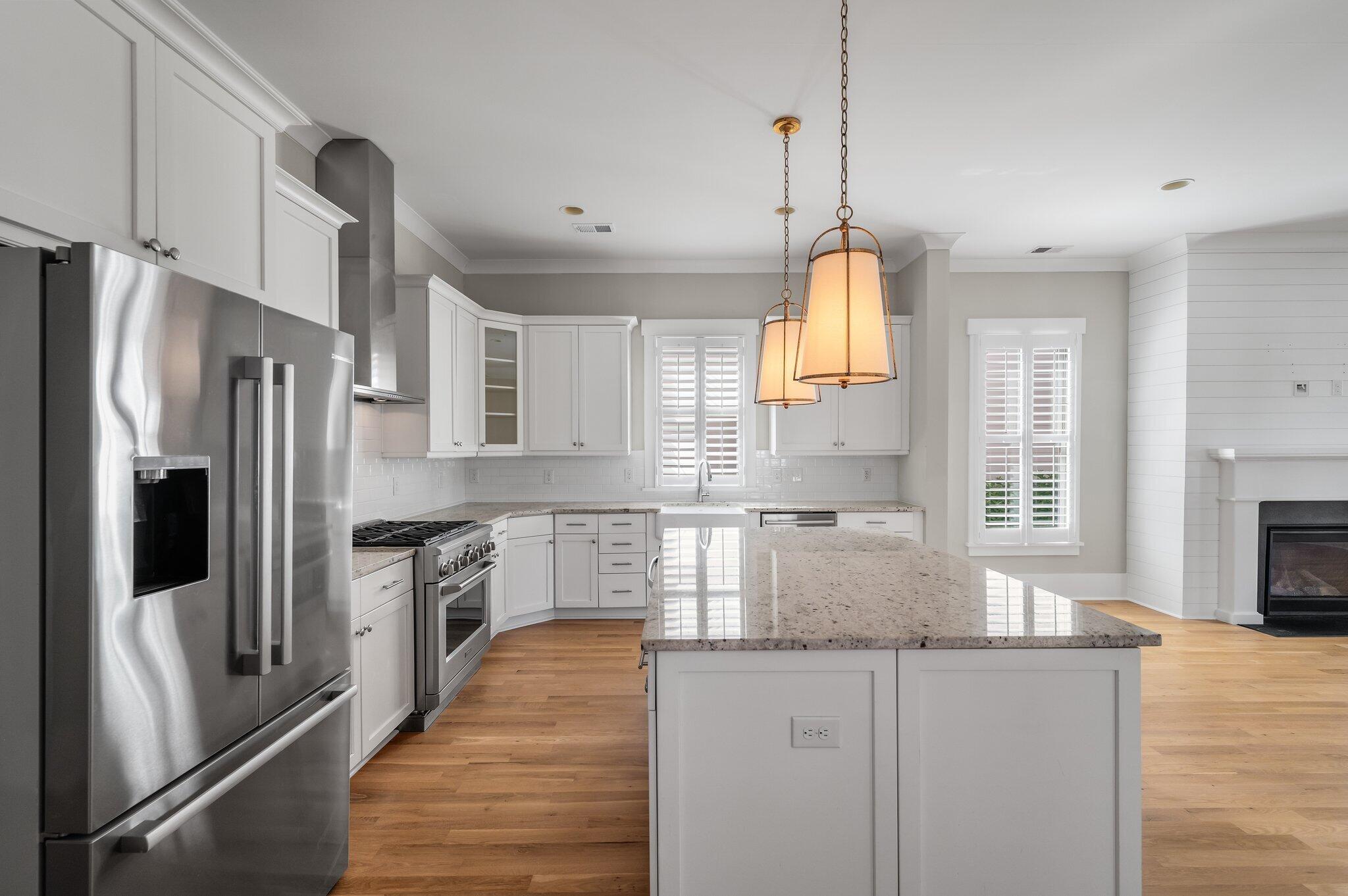 Bright kitchen with a large granite island, white cabinetry, stainless appliances, and pendant lights.