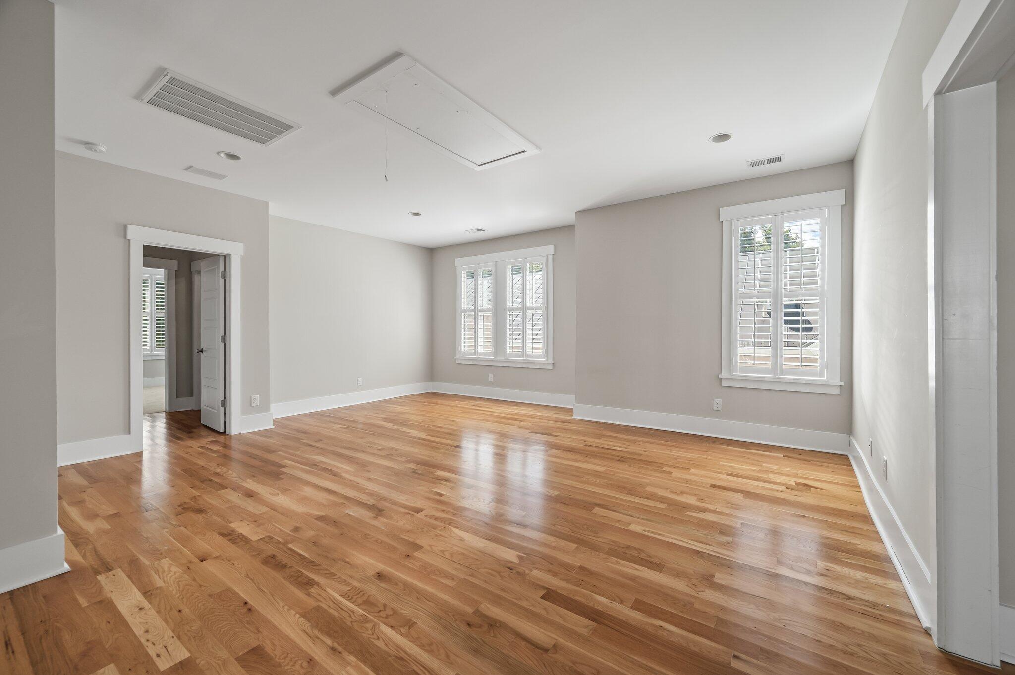 Empty room with hardwood floors, white trim, and shuttered windows.