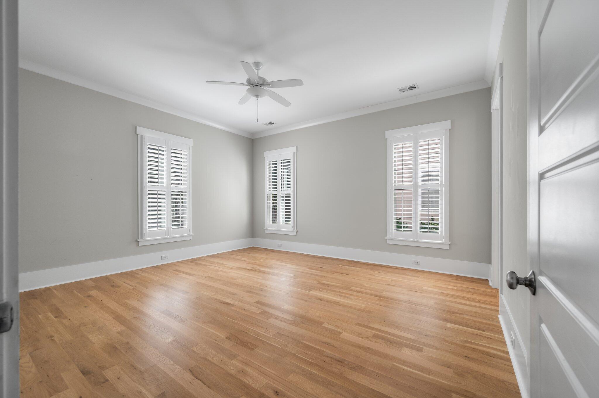 Empty room with hardwood floors, three shuttered windows, and a ceiling fan.