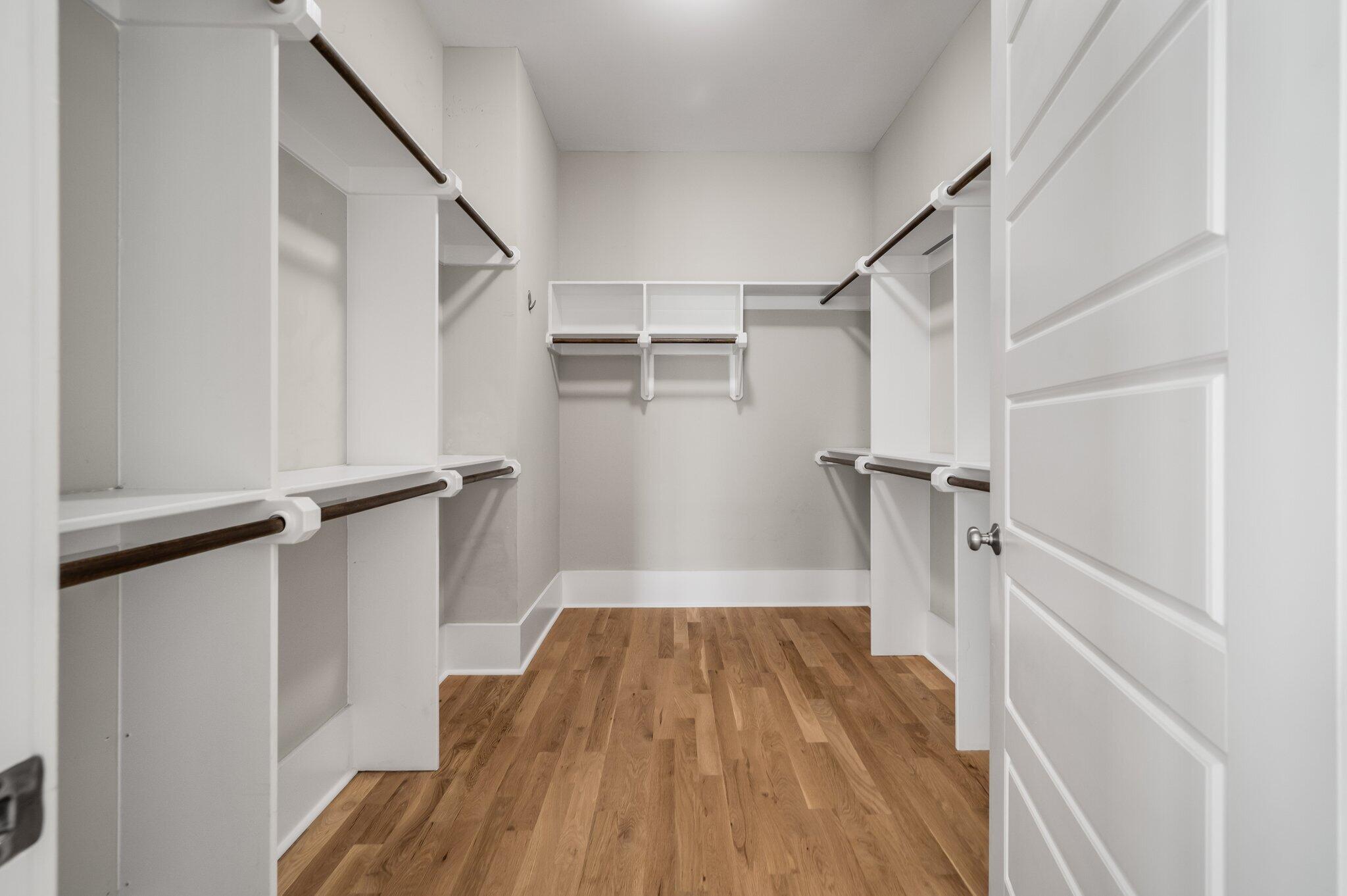Walk-in closet with built-in white shelving, dark hanging rods, and hardwood flooring.